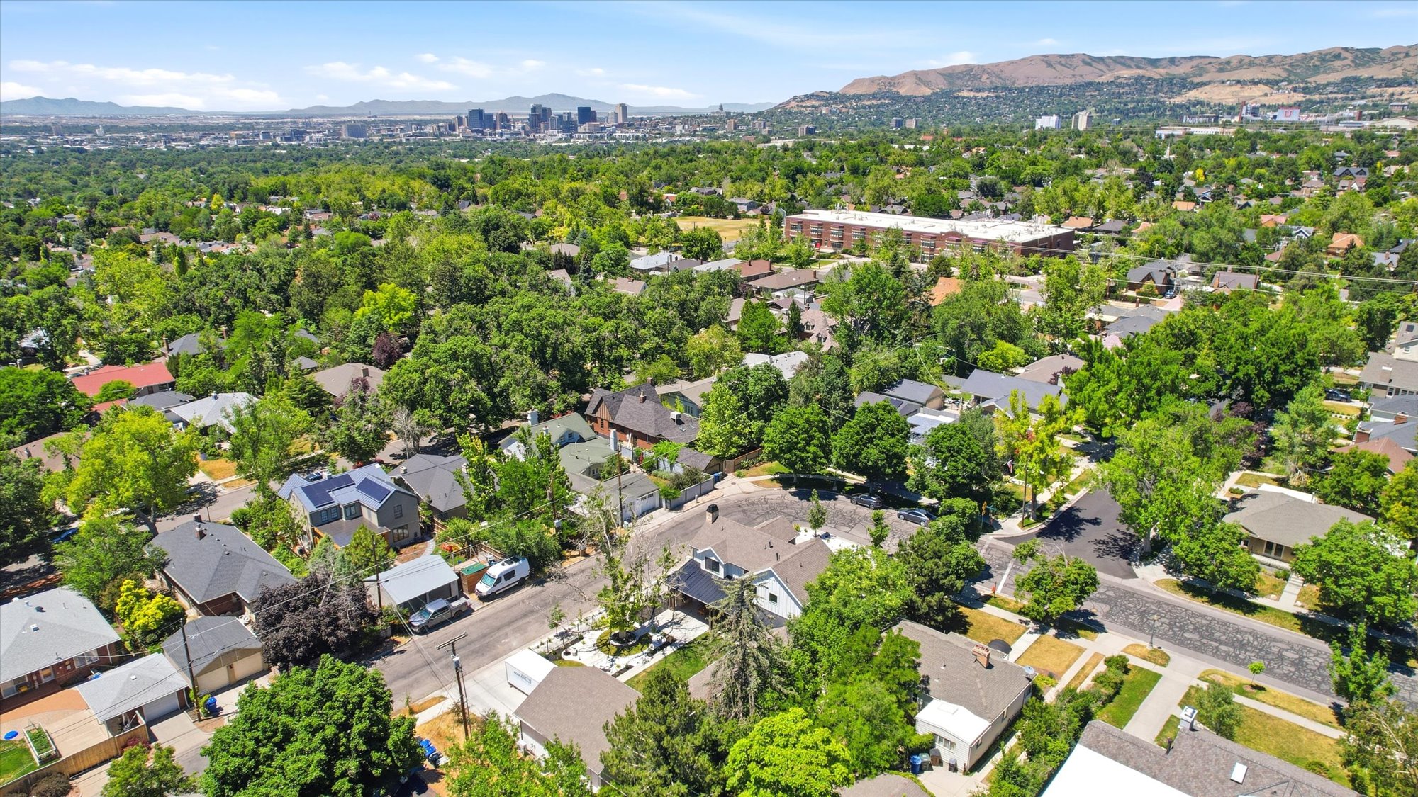 Expansive aerial landscape showcasing a residential neighborhood with abundant mature trees and mountainous terrain in the distance