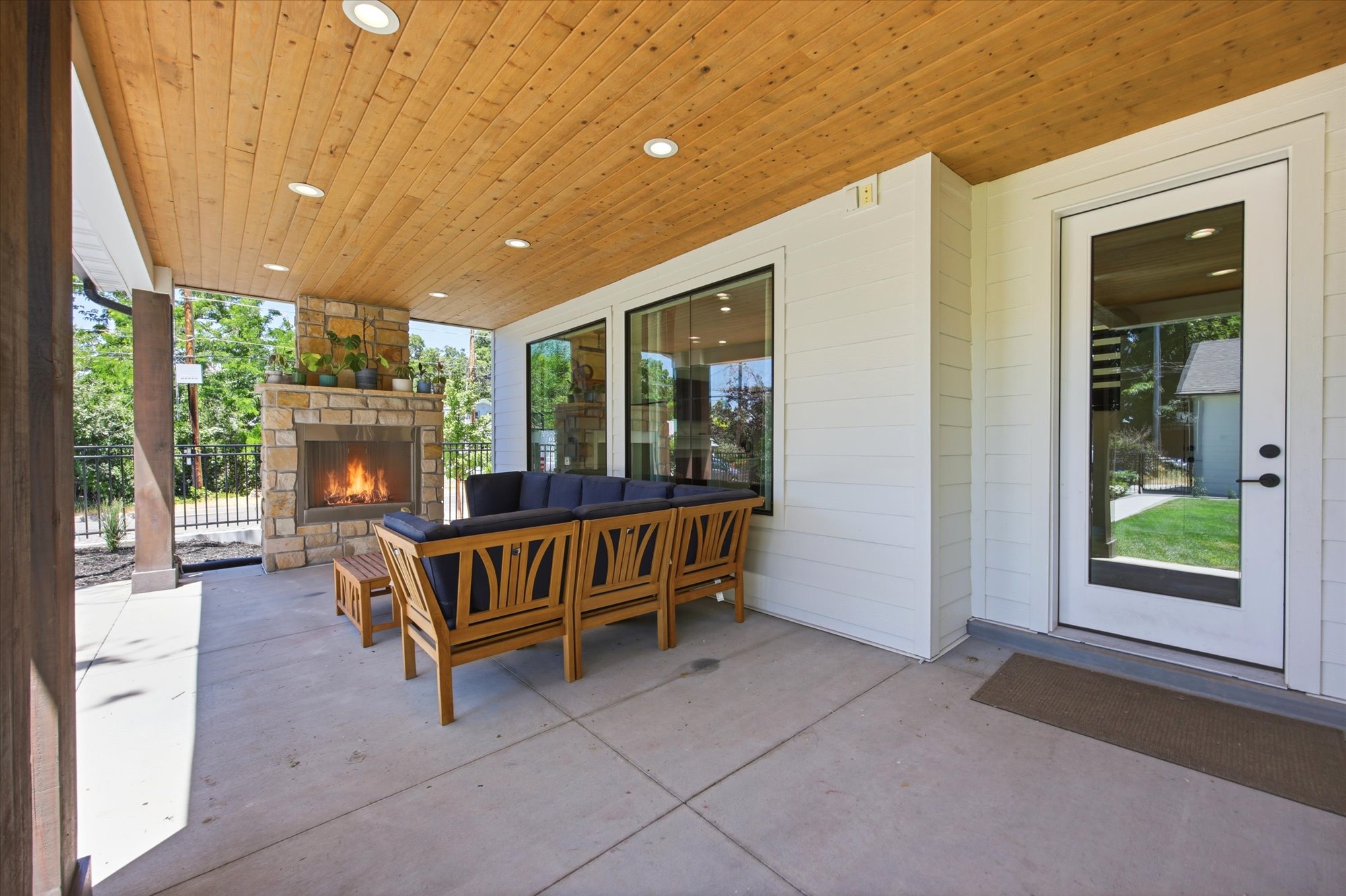 Covered patio featuring a stone fireplace, wood-plank ceiling with recessed lighting, and large glass windows