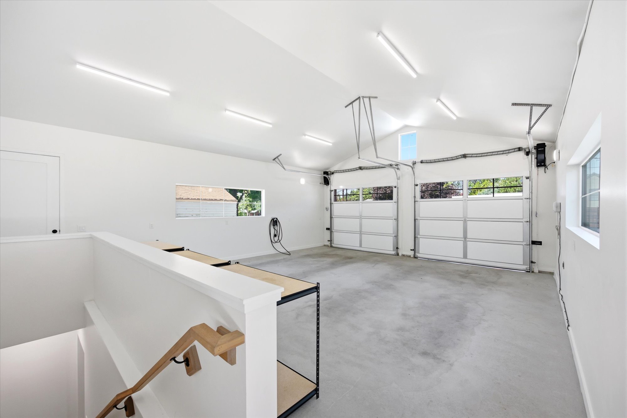 Spacious garage featuring two overhead doors with window panels, a vaulted ceiling, and multiple fluorescent light fixtures