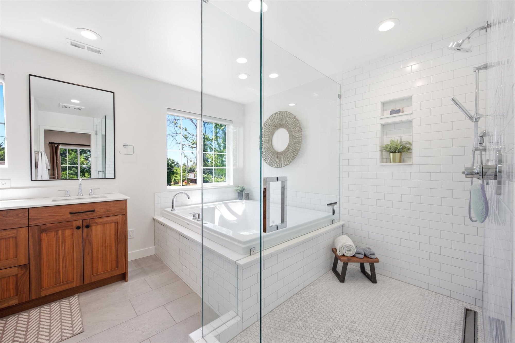Bathroom featuring a built-in soaking tub, glass-enclosed shower with subway tile surround, and a wood-finish vanity with a white countertop