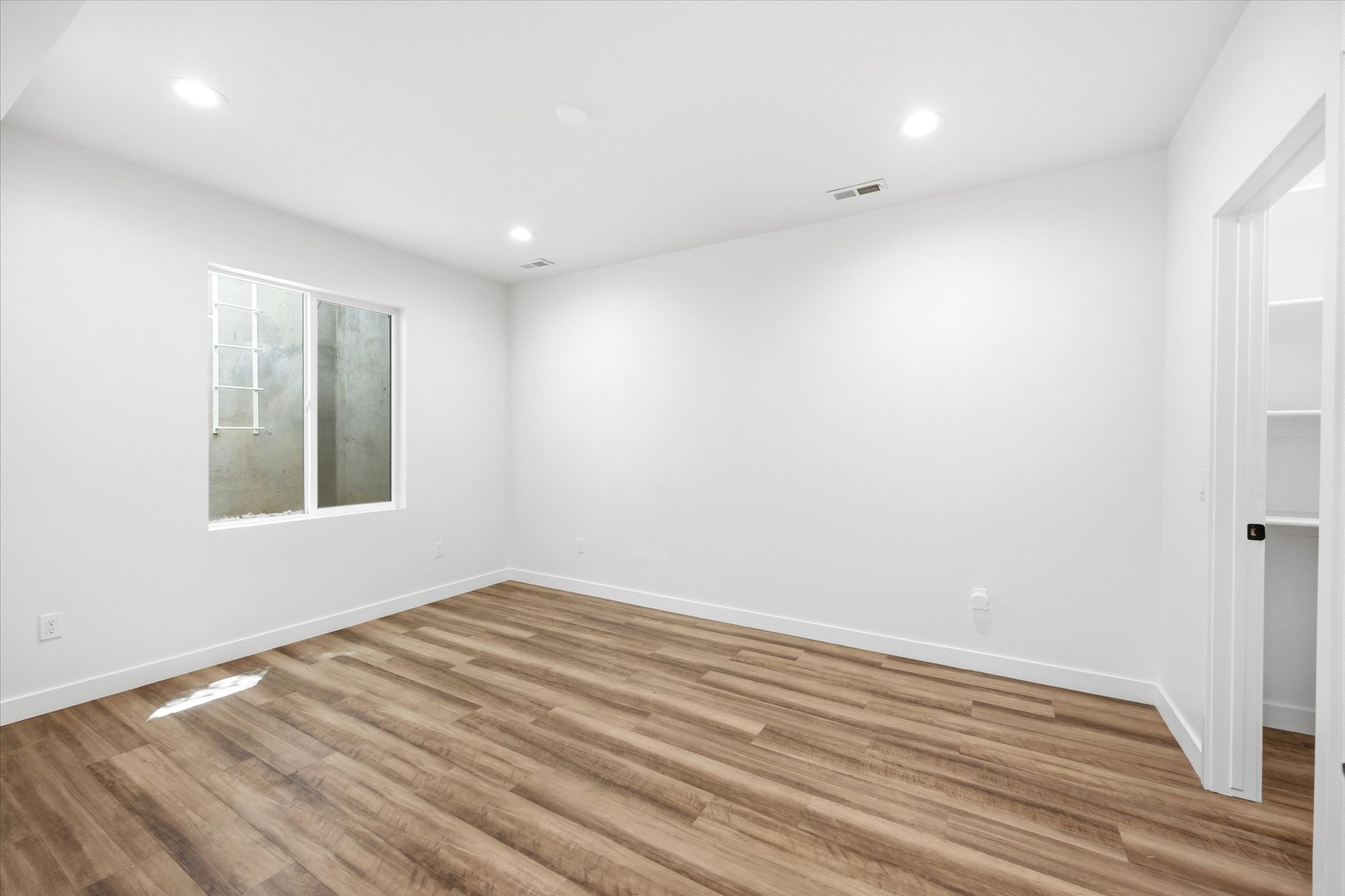 Spacious room featuring wood-finish flooring, recessed lighting, and a window with a security grate