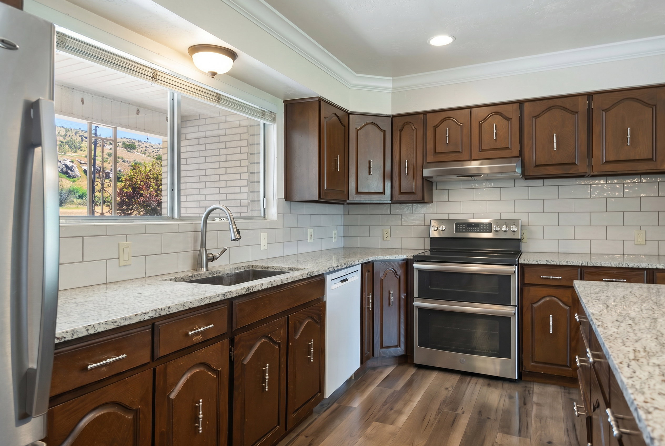 Kitchen featuring wood-finish flooring, wood cabinetry with brushed nickel hardware, and granite countertops
