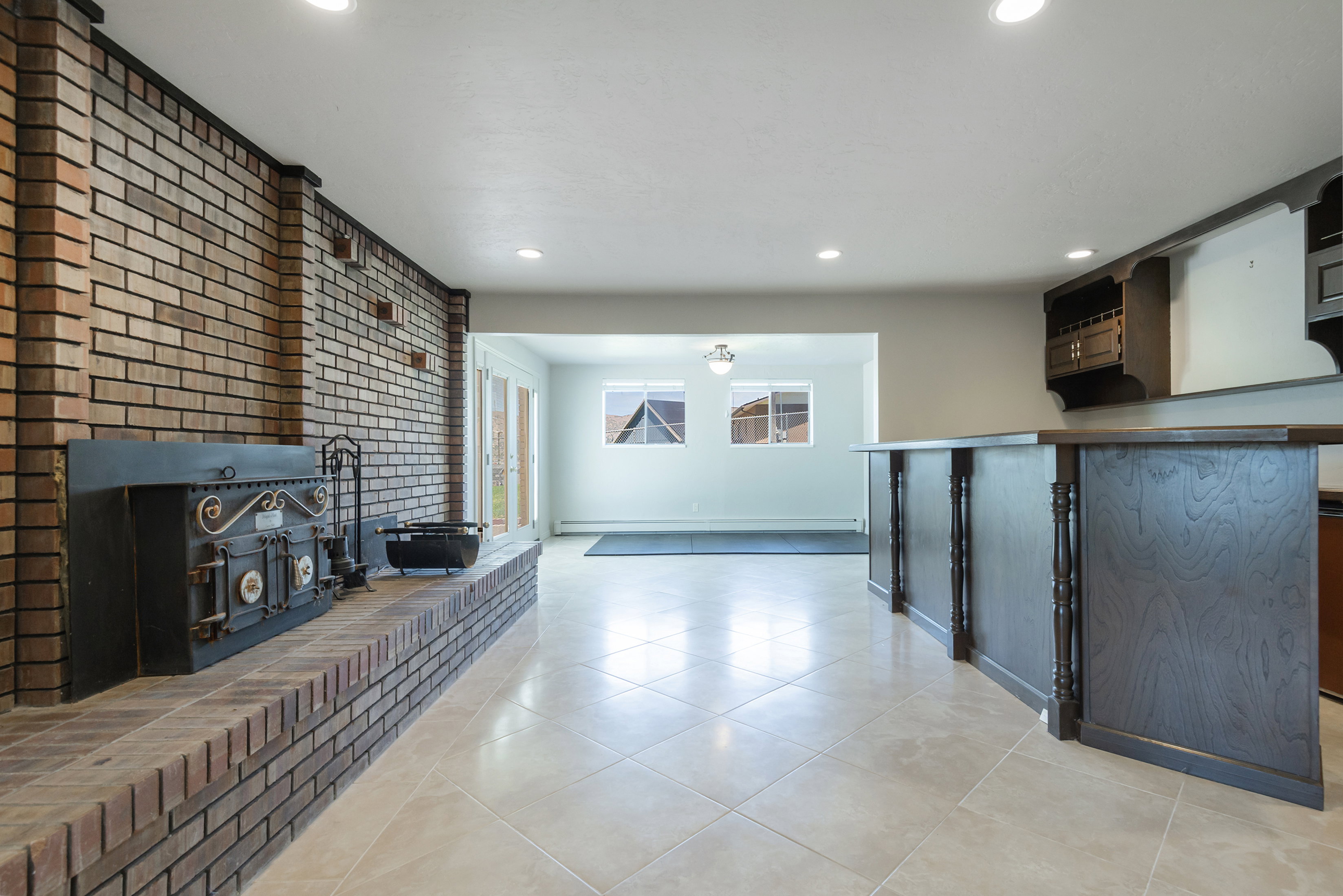 Expansive tiled flooring spans this versatile space, featuring a prominent brick fireplace with a decorative insert