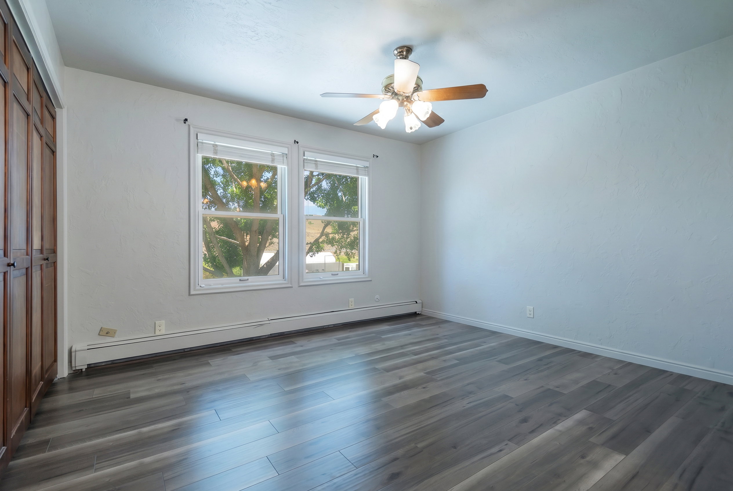 Spacious room featuring modern wood-finish flooring, dual windows, and built-in wood cabinetry