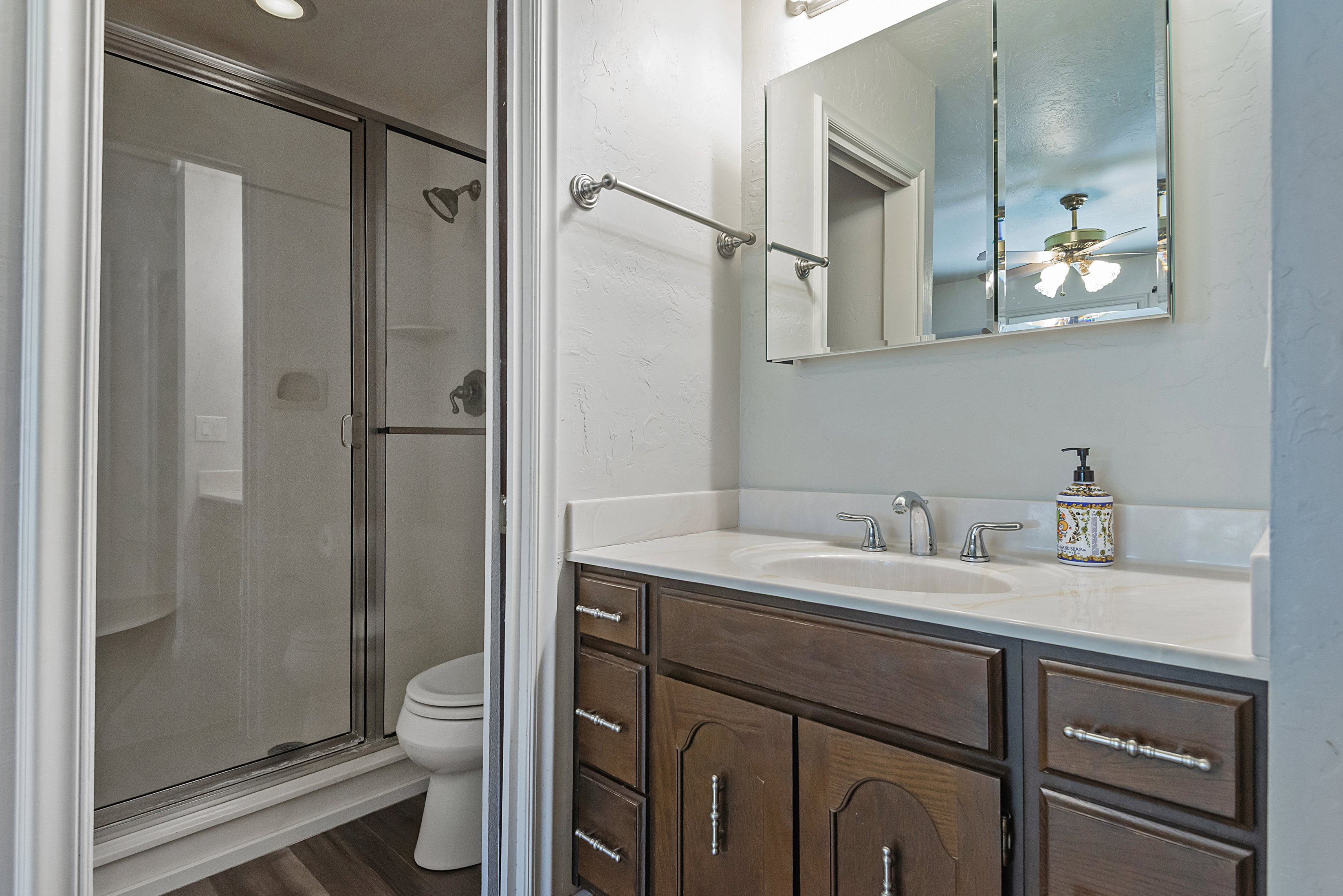 Bathroom featuring a glass-enclosed shower with integrated seating, wood-finish flooring, a vanity with a light-colored countertop, and a mirrored medicine cabinet