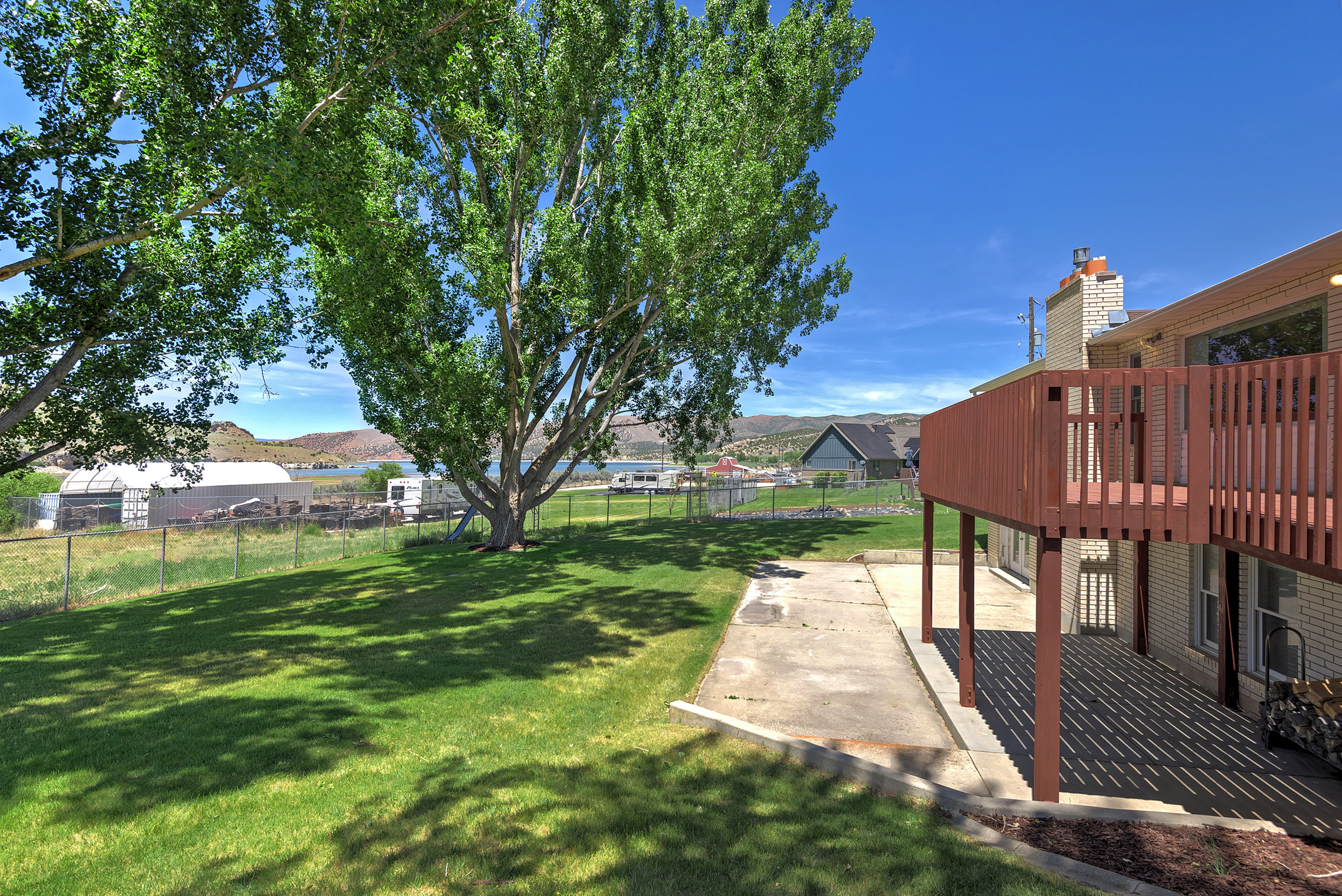Expansive backyard featuring a manicured lawn, mature trees, and a red-stained wood deck with a privacy screen