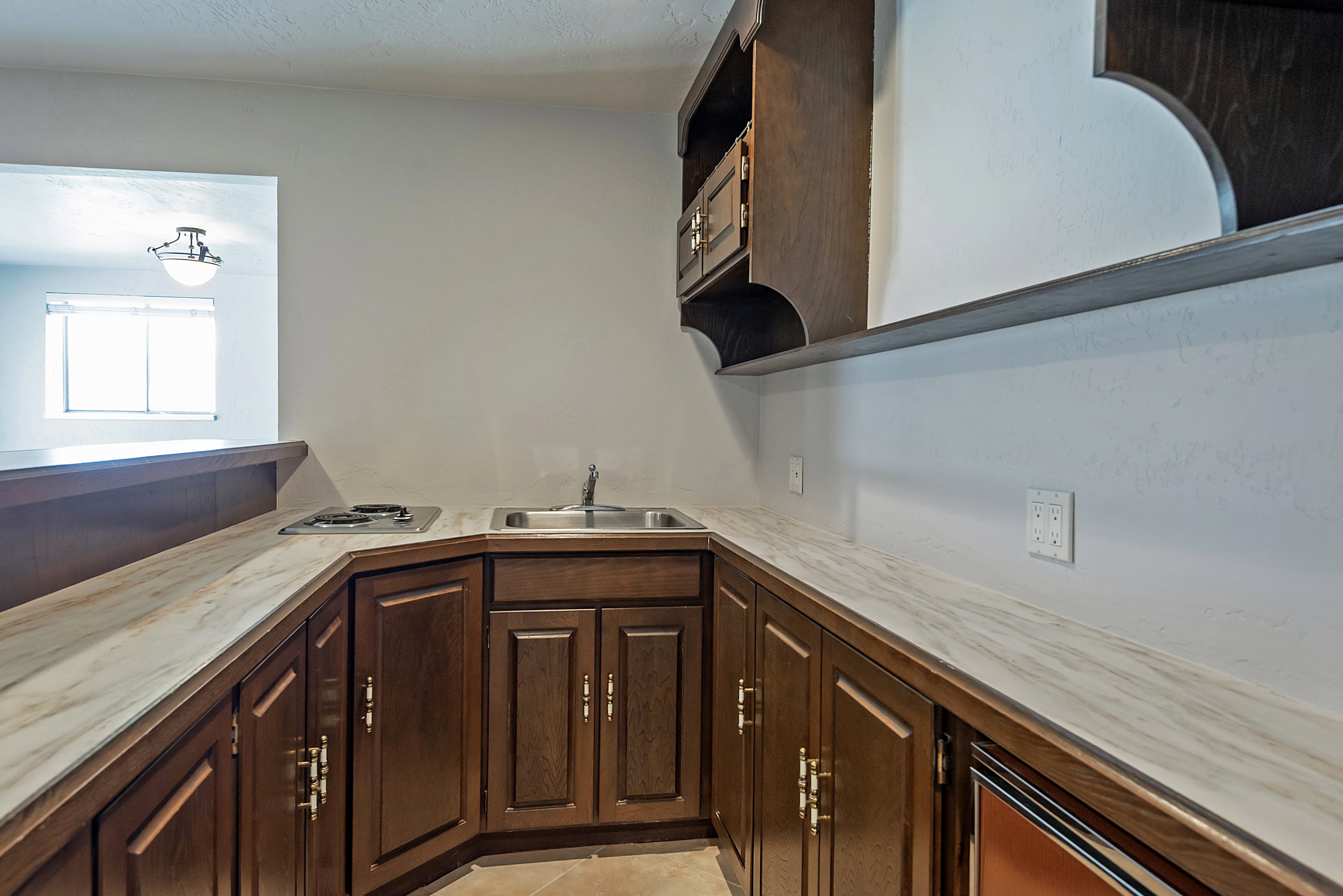 Compact wet bar with wood-finish cabinetry and light-toned, patterned countertops