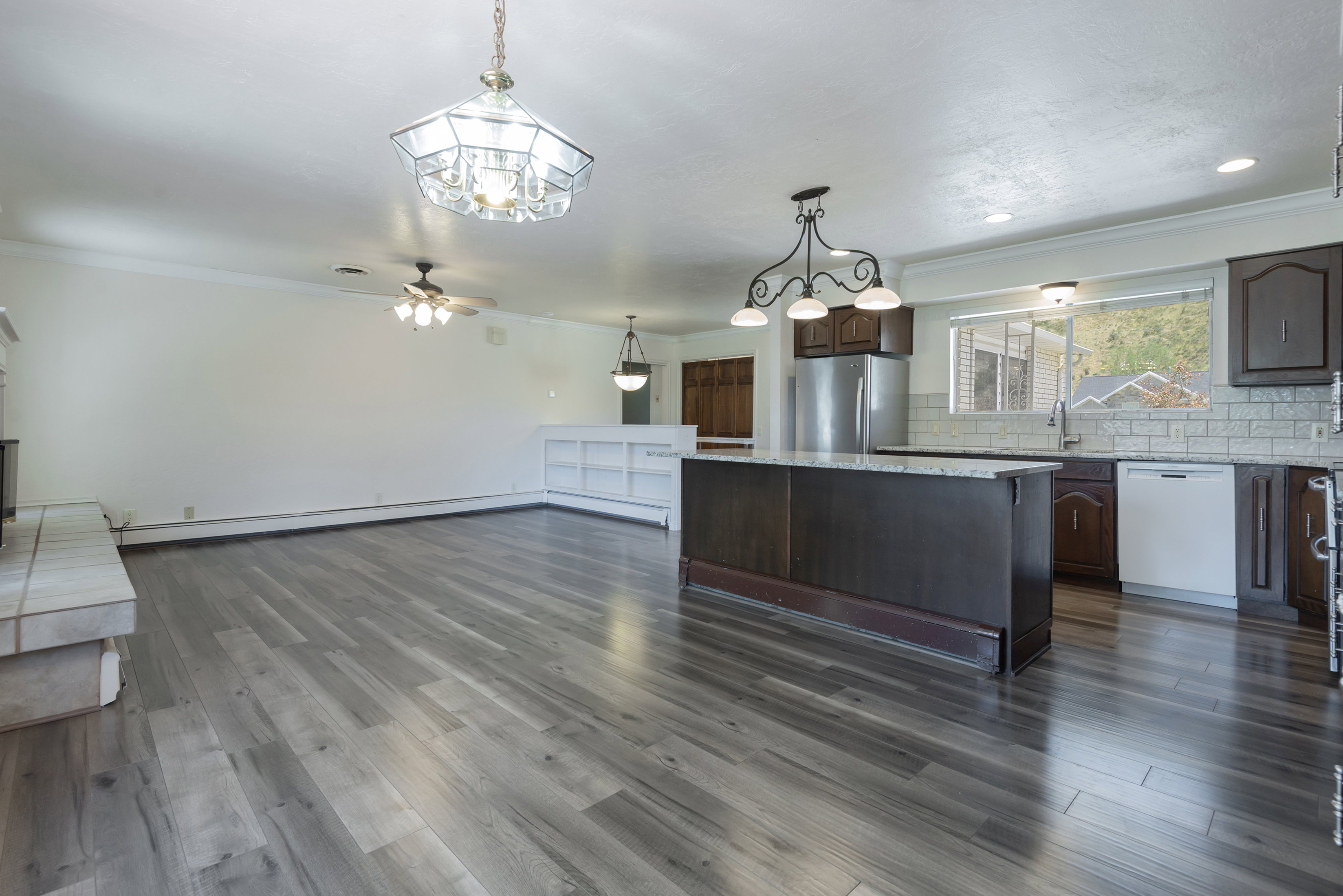 Expansive open-concept room featuring wood-finish flooring, a kitchen island with a stone countertop, dark wood cabinetry, and a subway tile backsplash