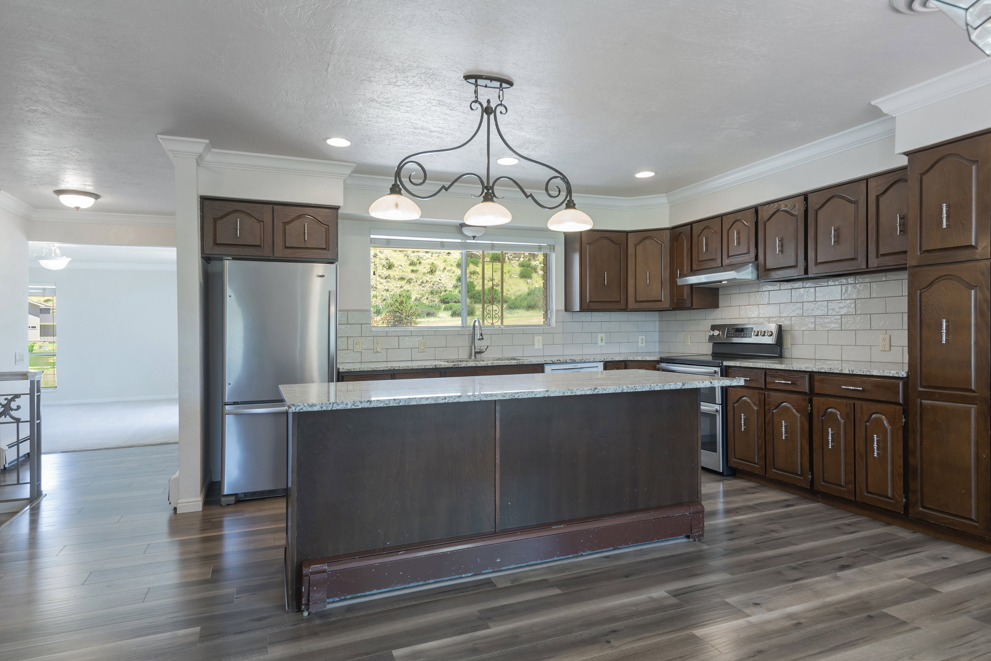 Kitchen featuring a central island with a light-toned countertop, wood-finish flooring, dark wood cabinetry, a subway tile backsplash, and stainless steel appliances