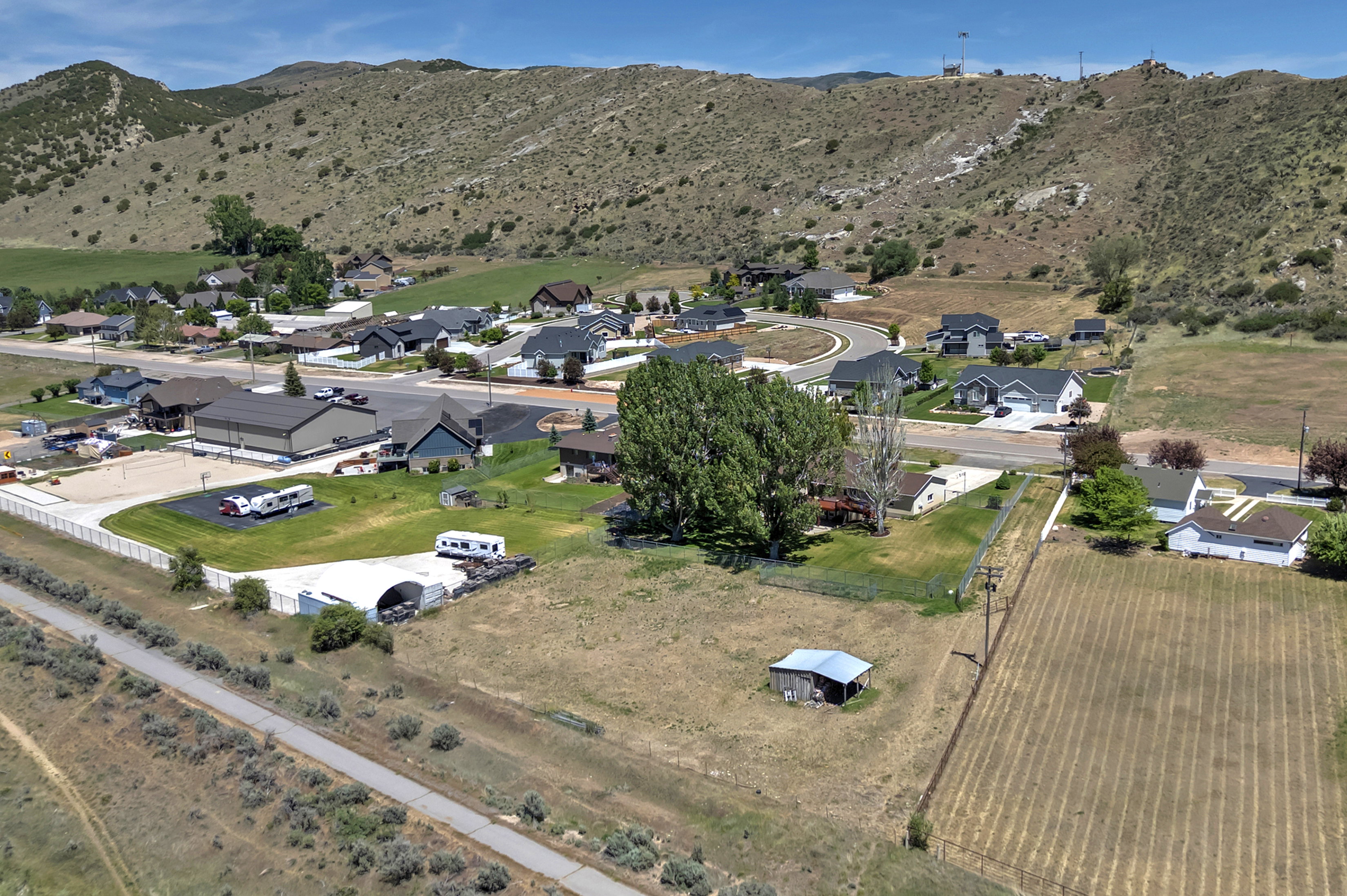 Expansive land parcel featuring open fields, a small outbuilding, and mature trees, surrounded by residential development and natural hills