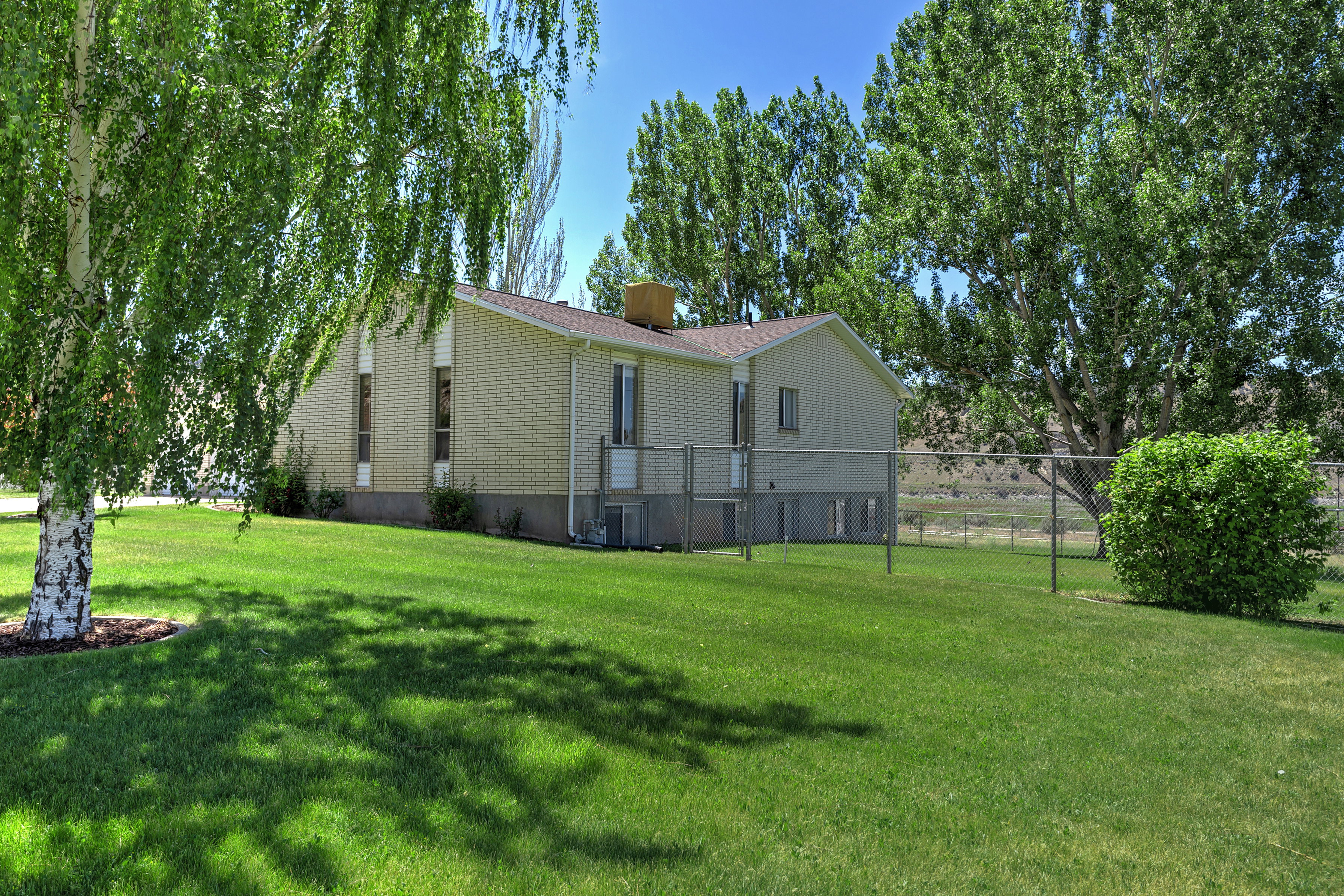 Expansive green lawn with mature trees and a chain-link fence