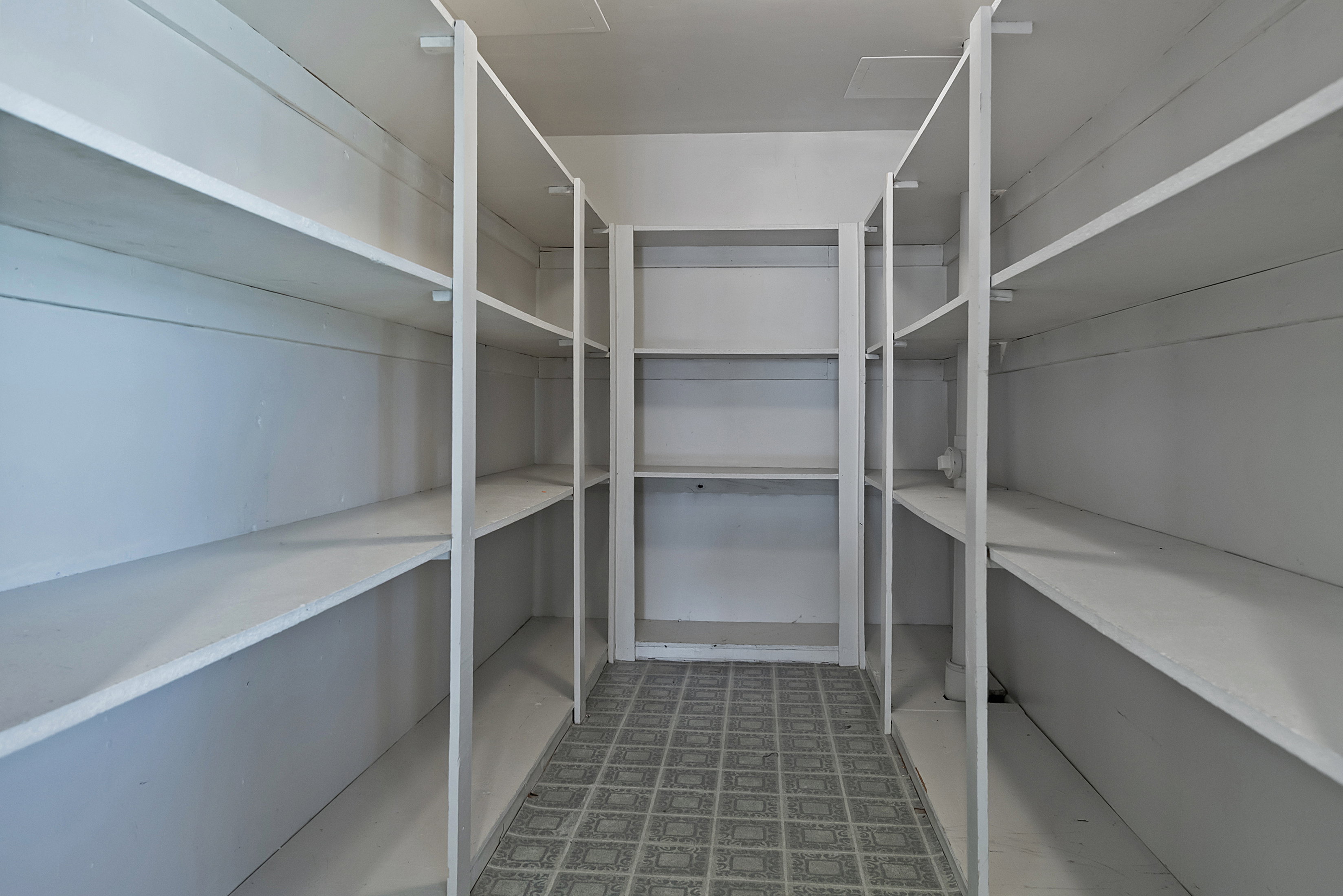 Walk-in pantry featuring extensive white shelving along three walls, providing abundant storage capacity