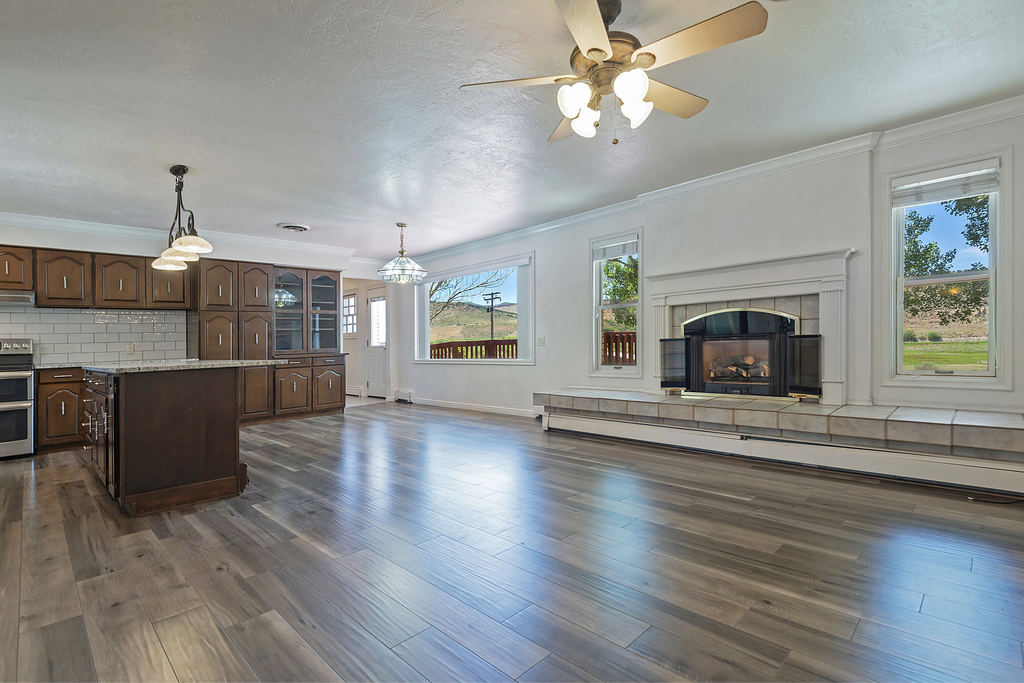 Spacious interior featuring wood-finish flooring, a kitchen island with stone-finish countertop, a fireplace with a tiled hearth and surround, and multiple windows providing natural light
