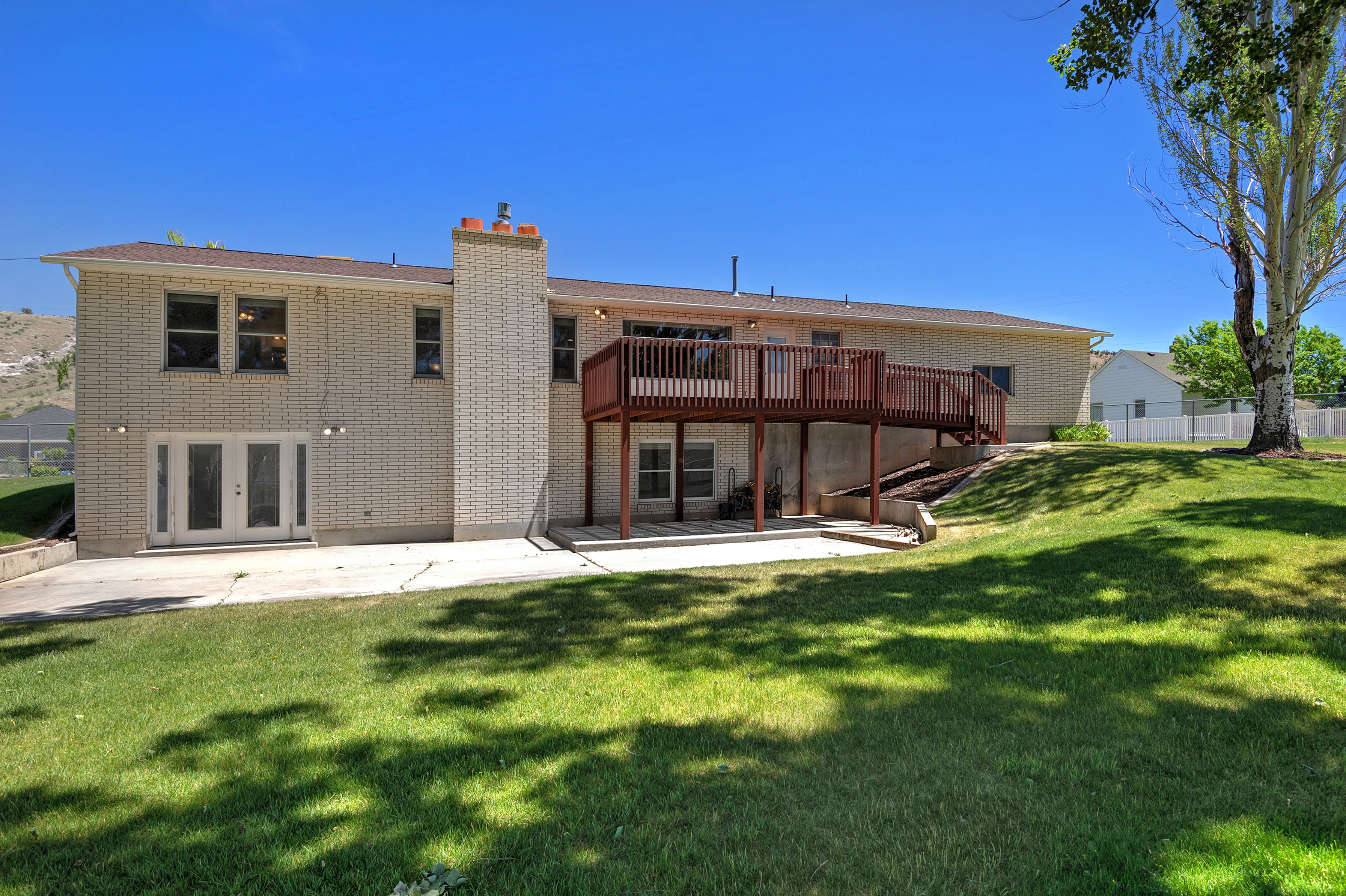 Rear exterior featuring a spacious elevated deck, brick facade, ground-level patio, and a large grassy yard