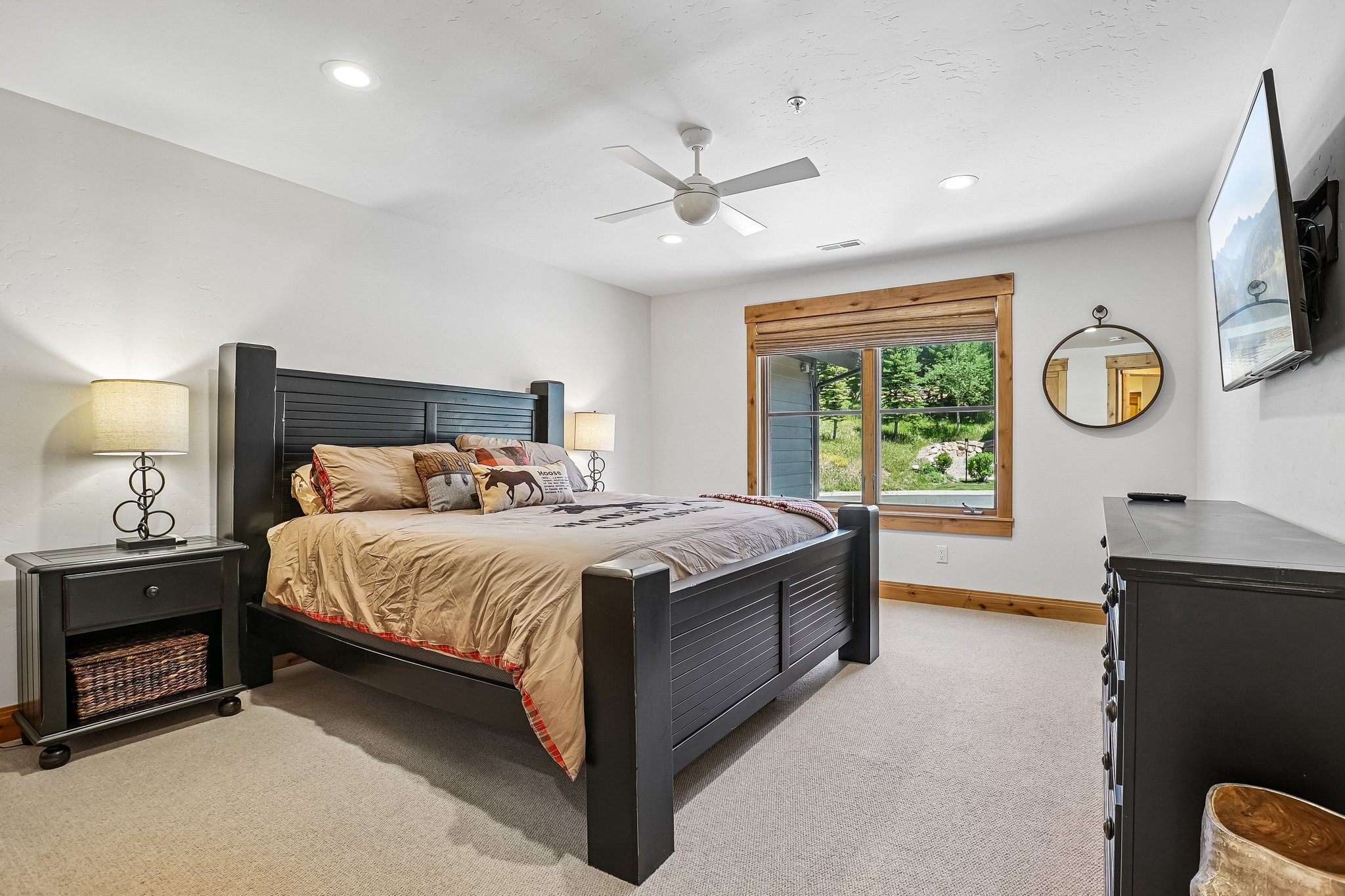 Spacious room featuring carpeted flooring, a ceiling fan, recessed lighting, a large window with natural wood trim, and a wall-mounted mirror