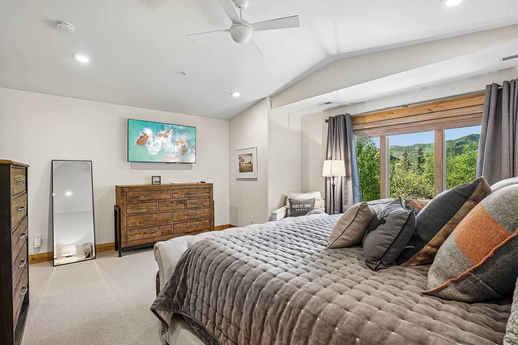 Spacious bedroom featuring vaulted ceilings, recessed lighting, a ceiling fan, and large windows with integrated wood trim