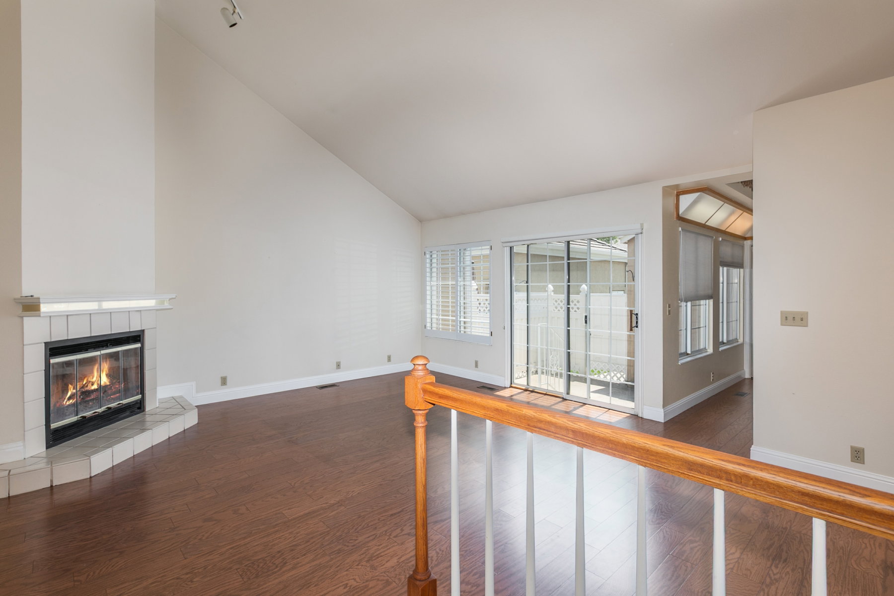 Spacious living area featuring vaulted ceilings, wood-finish flooring, a corner fireplace with a tiled hearth, and large sliding glass doors providing outdoor access