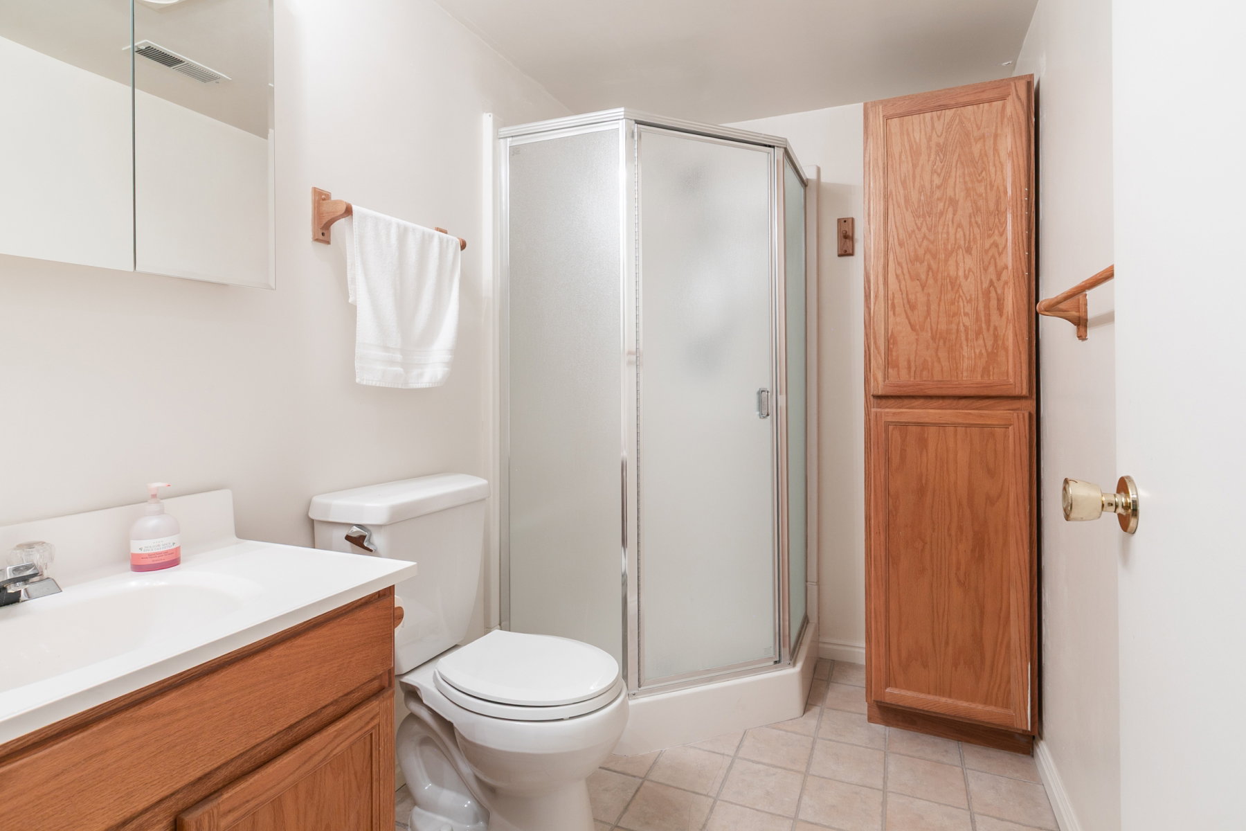 Bathroom featuring a corner shower enclosure with frosted glass, a vanity with wood-finish cabinetry, a built-in linen cabinet with wood-finish doors, a wall-mounted medicine cabinet with mirrored doors, and ceramic tile flooring