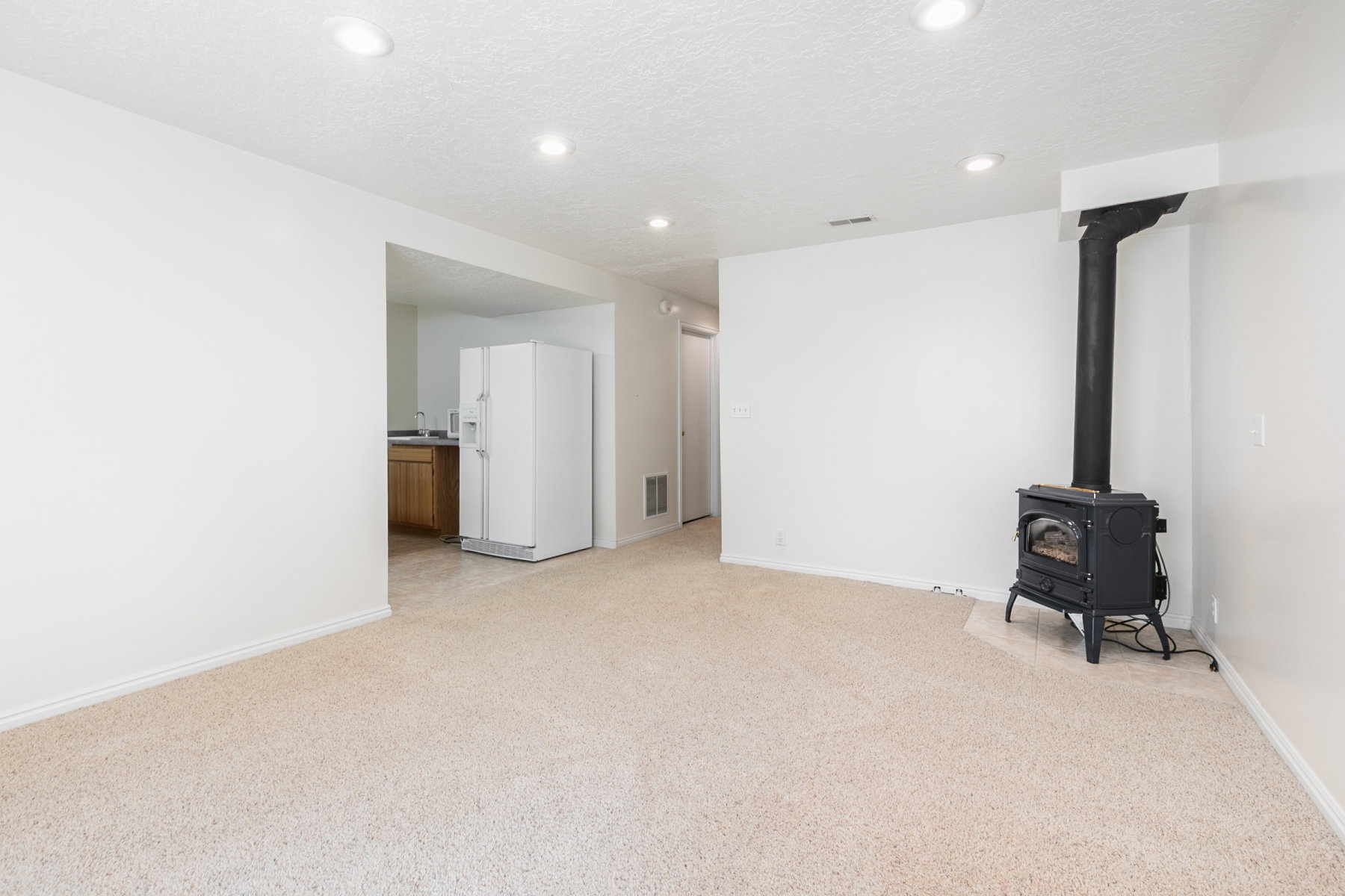 Carpeted living area with a black freestanding stove, recessed lighting, and white baseboards
