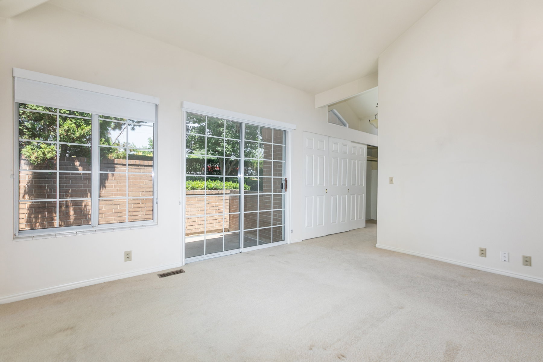 Carpeted interior space featuring a large window with white grilles, a sliding glass door with white grilles, and a vaulted ceiling