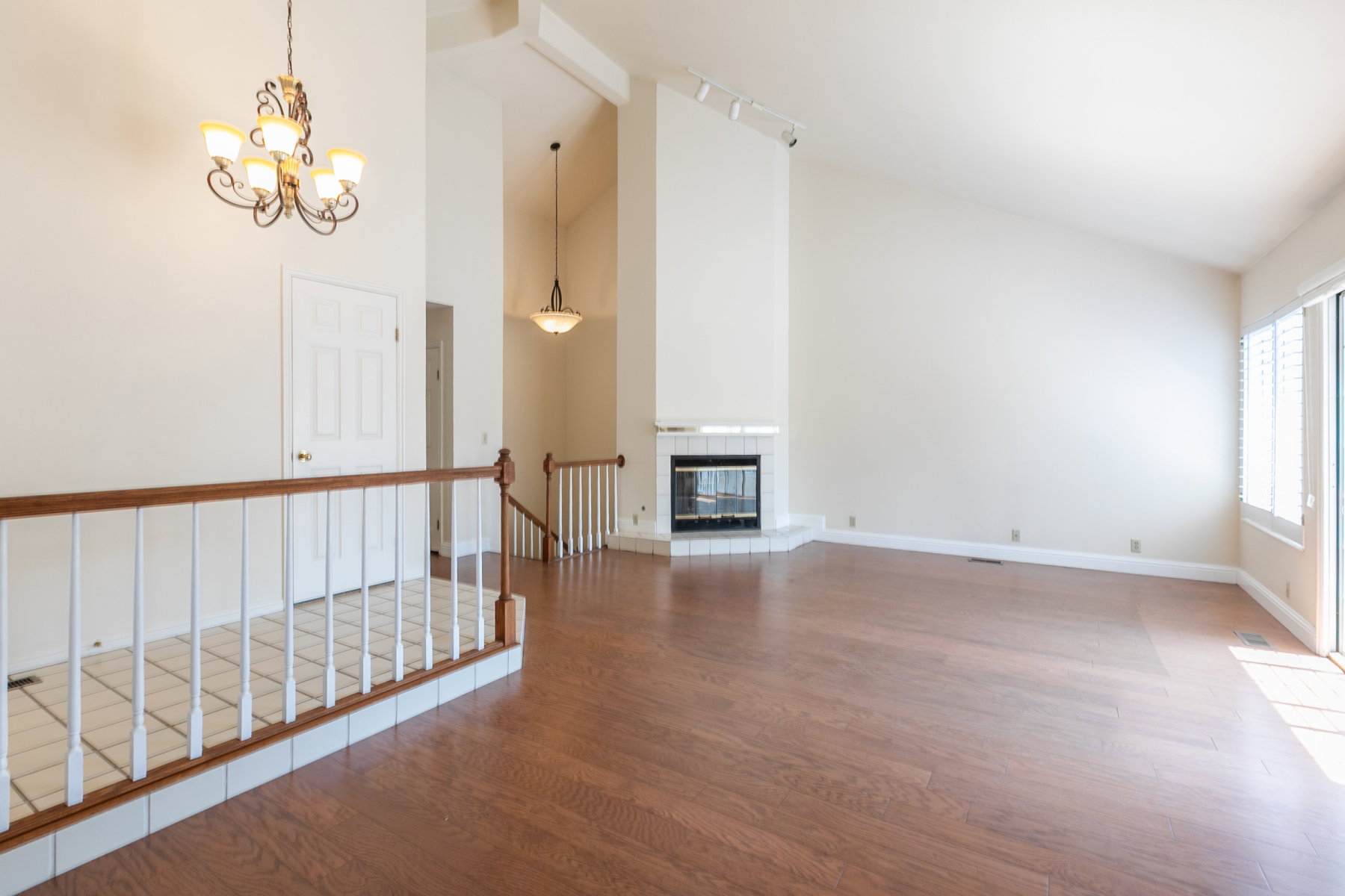 Spacious interior featuring wood-finish flooring, a white tile fireplace, and vaulted ceilings