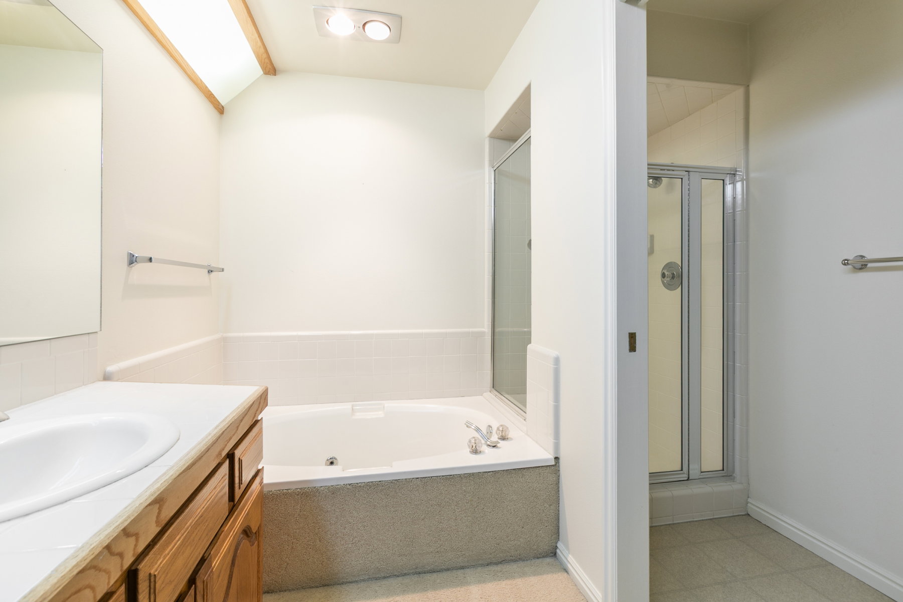 Bathroom featuring a built-in soaking tub, a separate glass-enclosed shower, a wood-finish vanity with an integrated sink, and overhead lighting