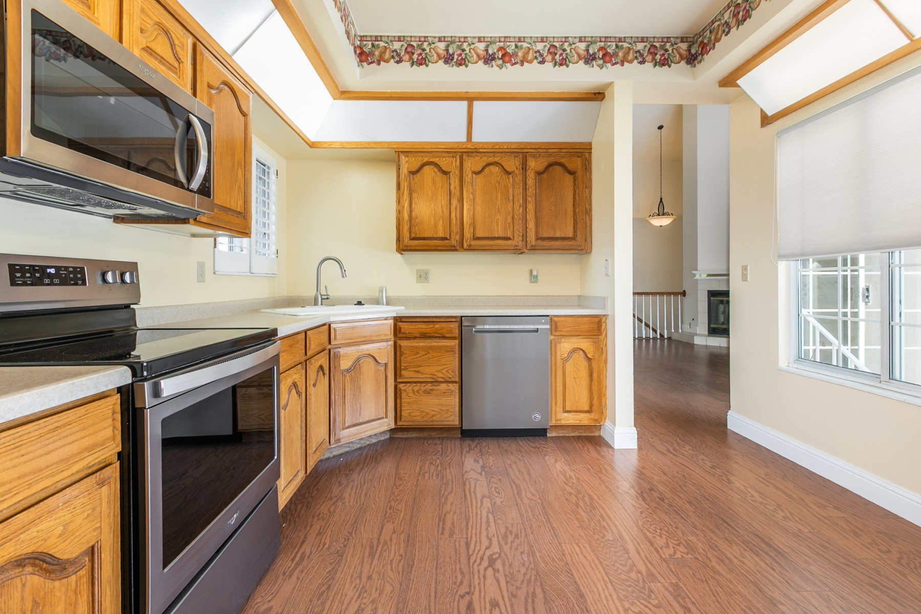 Kitchen featuring wood-finish flooring, oak cabinetry, stainless steel appliances, and skylights
