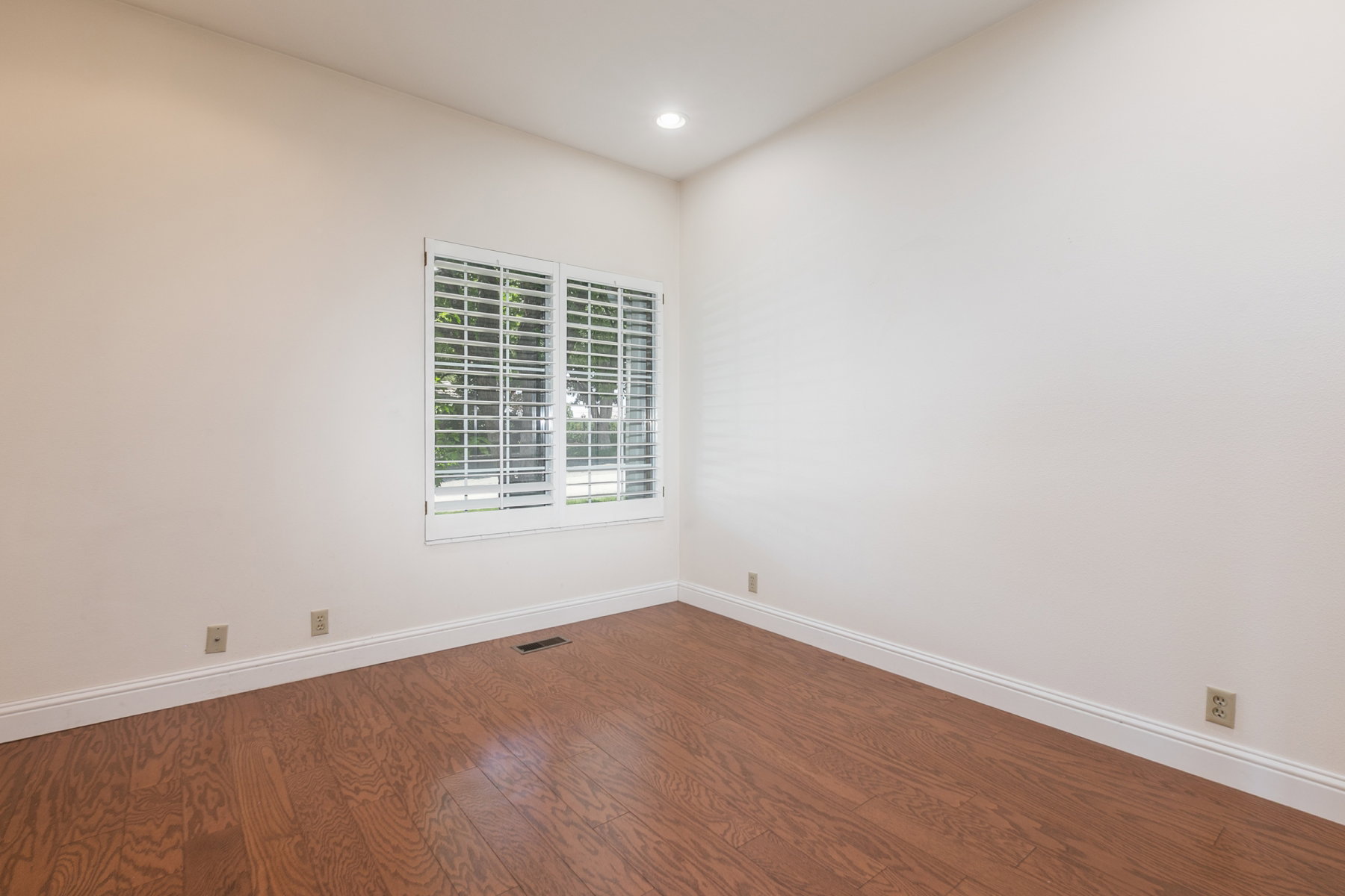 Room with wood-finish flooring, white walls, and white plantation shutters on the window
