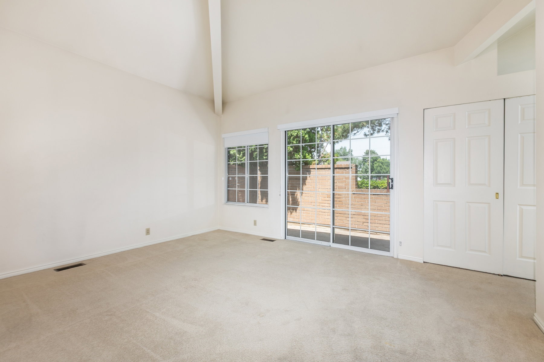 Vaulted ceiling with exposed beam, beige carpeting, large sliding glass door, single grid window, and bi-fold closet doors