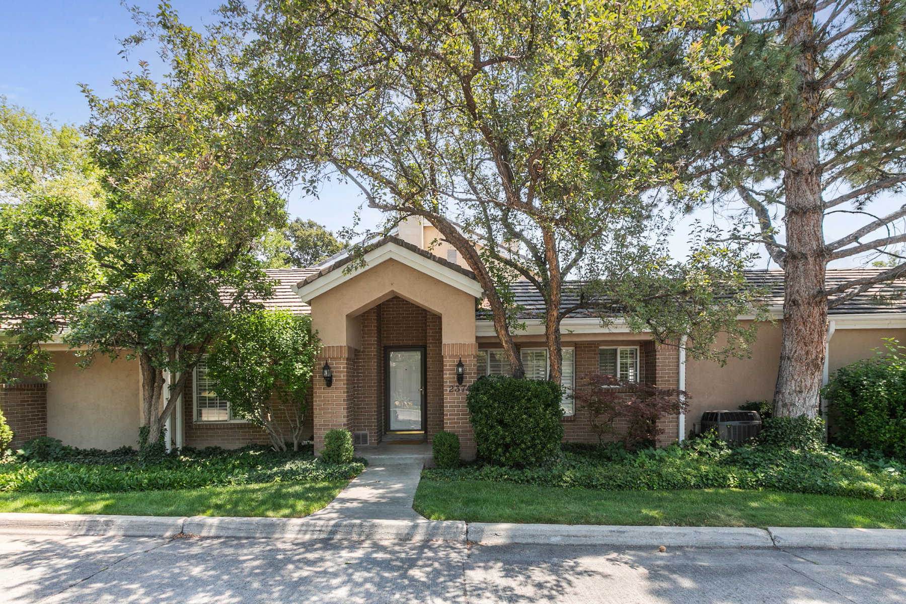 Exterior facade featuring a covered entryway with brick accents, mature trees, and established landscaping