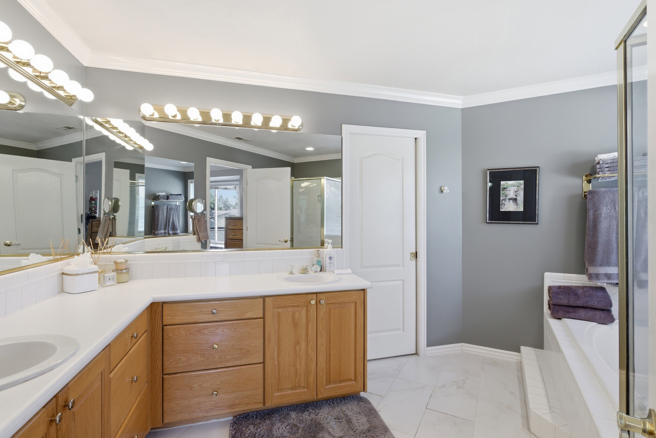 Bathroom featuring a dual vanity with light wood cabinetry, white countertops, and a large wall-mounted mirror