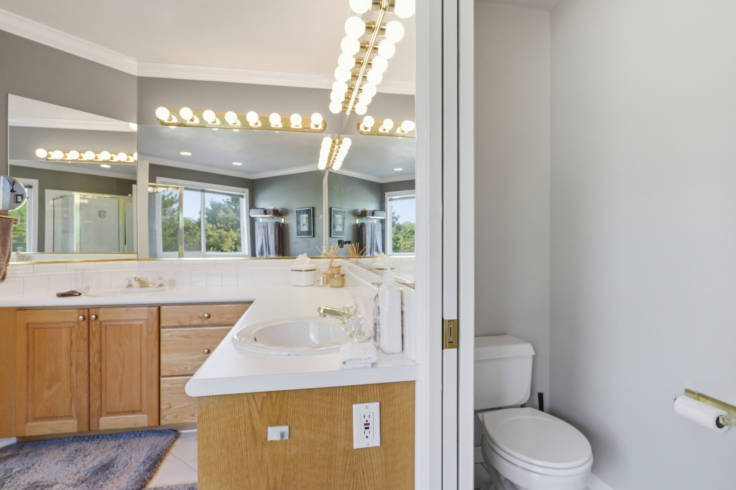 Dual vanity with integrated sinks, white countertops, extensive mirror, and wood-finish cabinetry