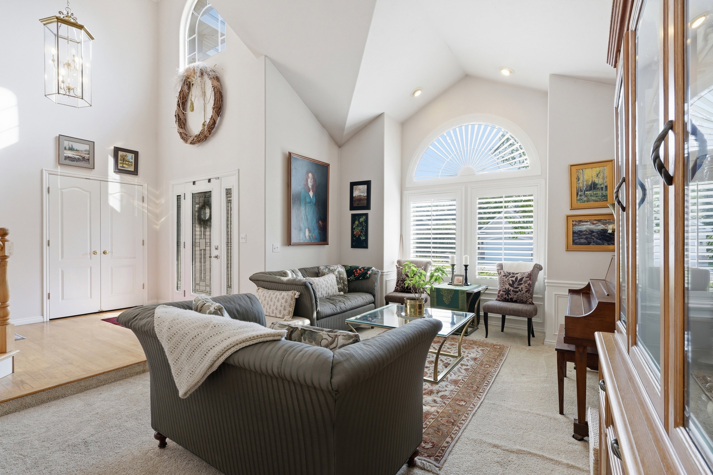 Living area featuring vaulted ceilings, a large arched window with plantation shutters, recessed lighting, and wood-finish flooring