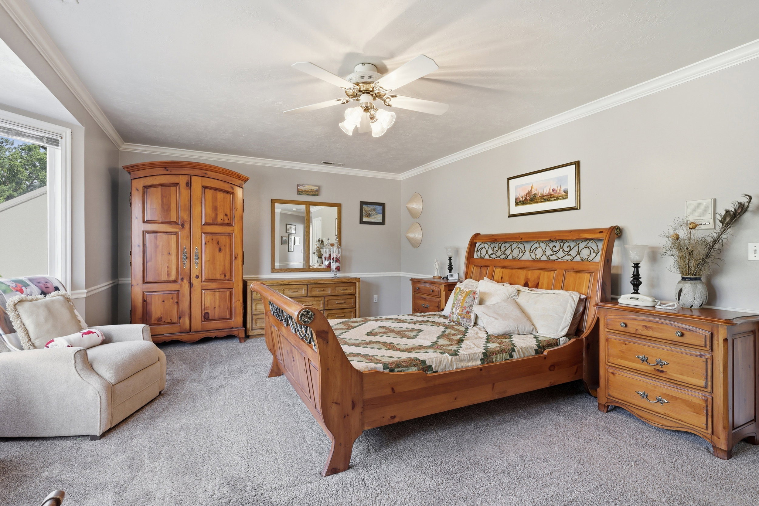 Spacious room featuring neutral carpeting, a large bay window, crown molding, and a ceiling fan