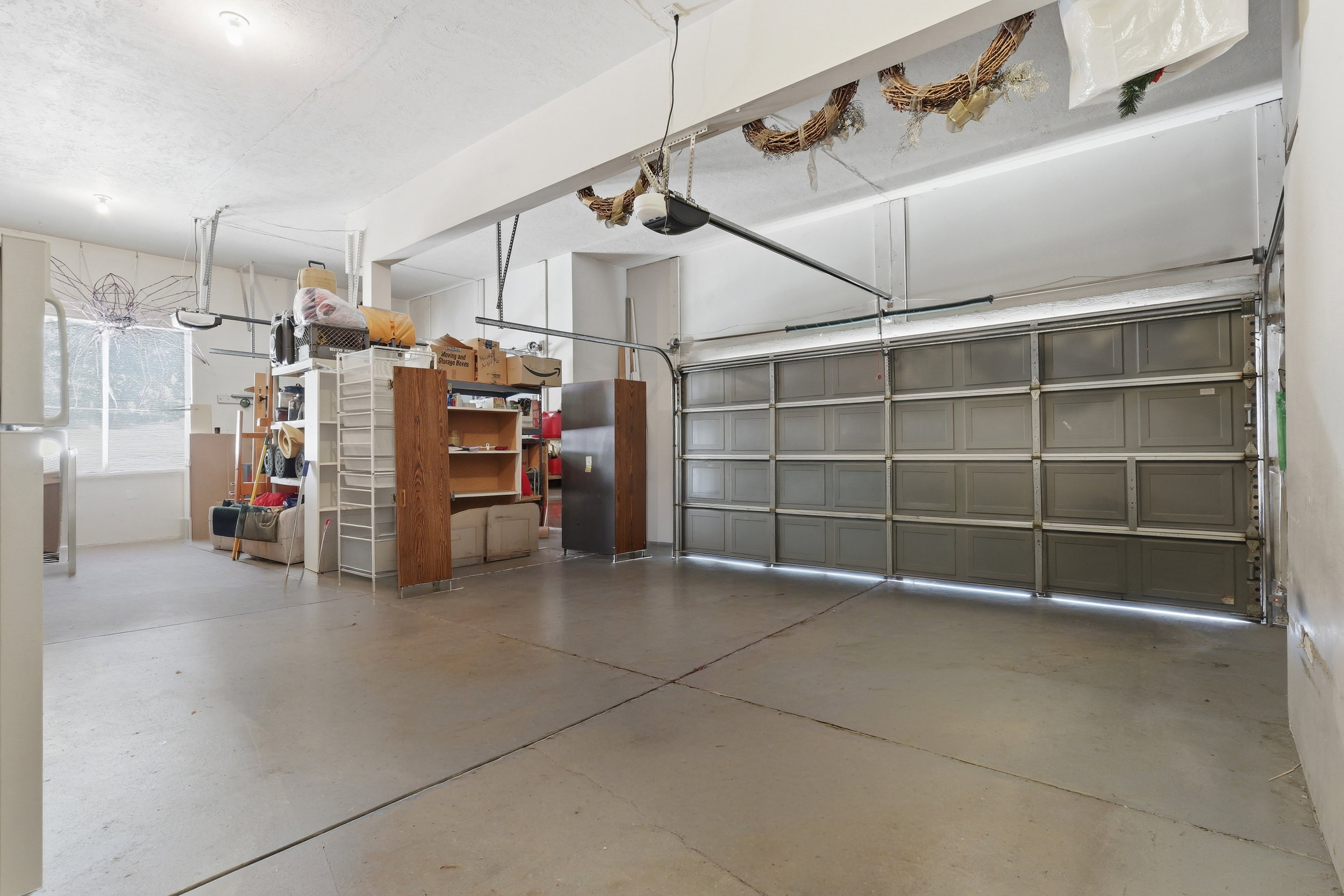 Spacious garage featuring a concrete floor, overhead lighting, garage door mechanism, and a window providing natural light