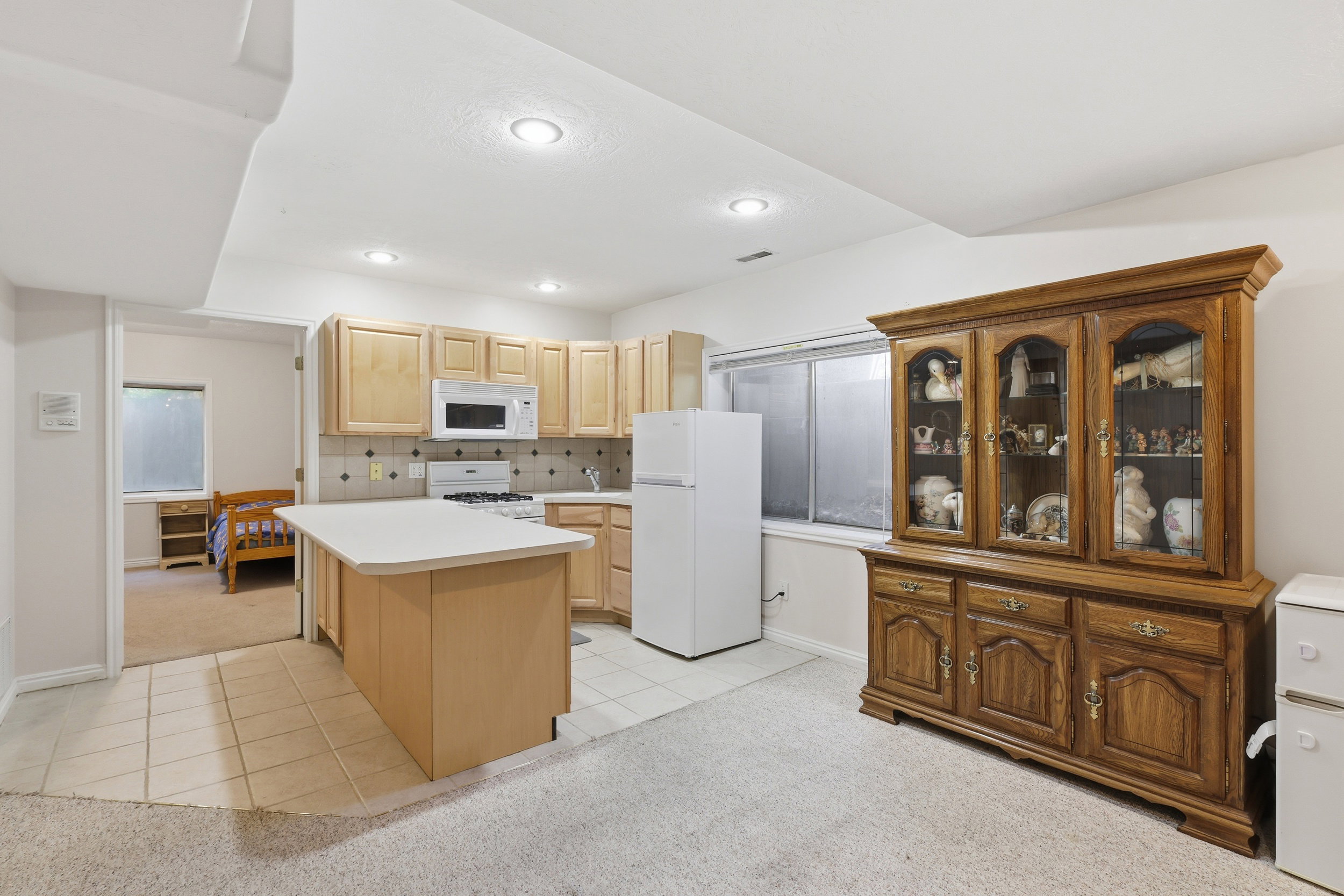 Kitchenette featuring light wood-finish cabinetry, white appliances, a tile backsplash, and an island with countertop seating