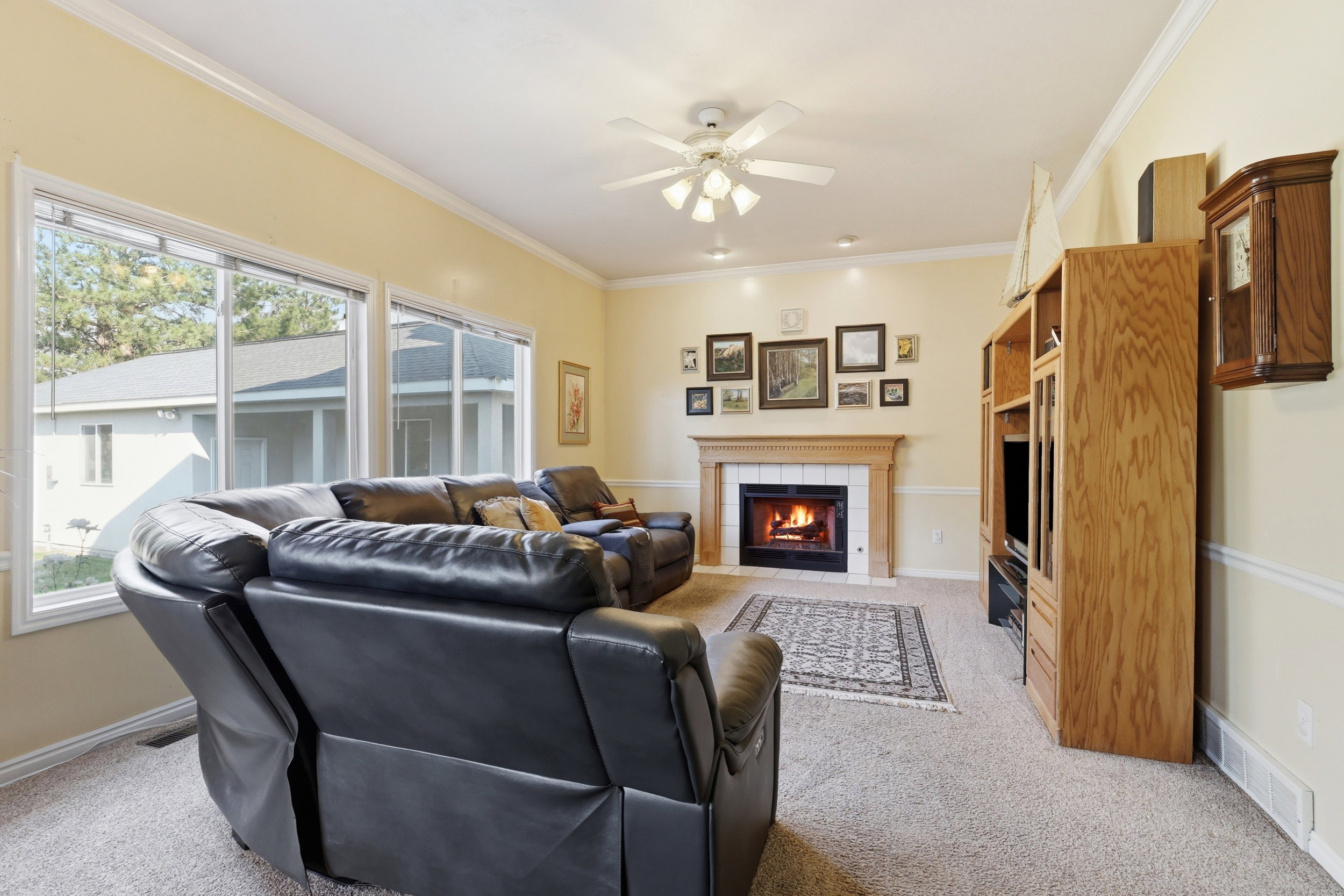 Living area featuring a fireplace with a wood mantel, multiple windows, recessed lighting, crown molding, and a ceiling fan