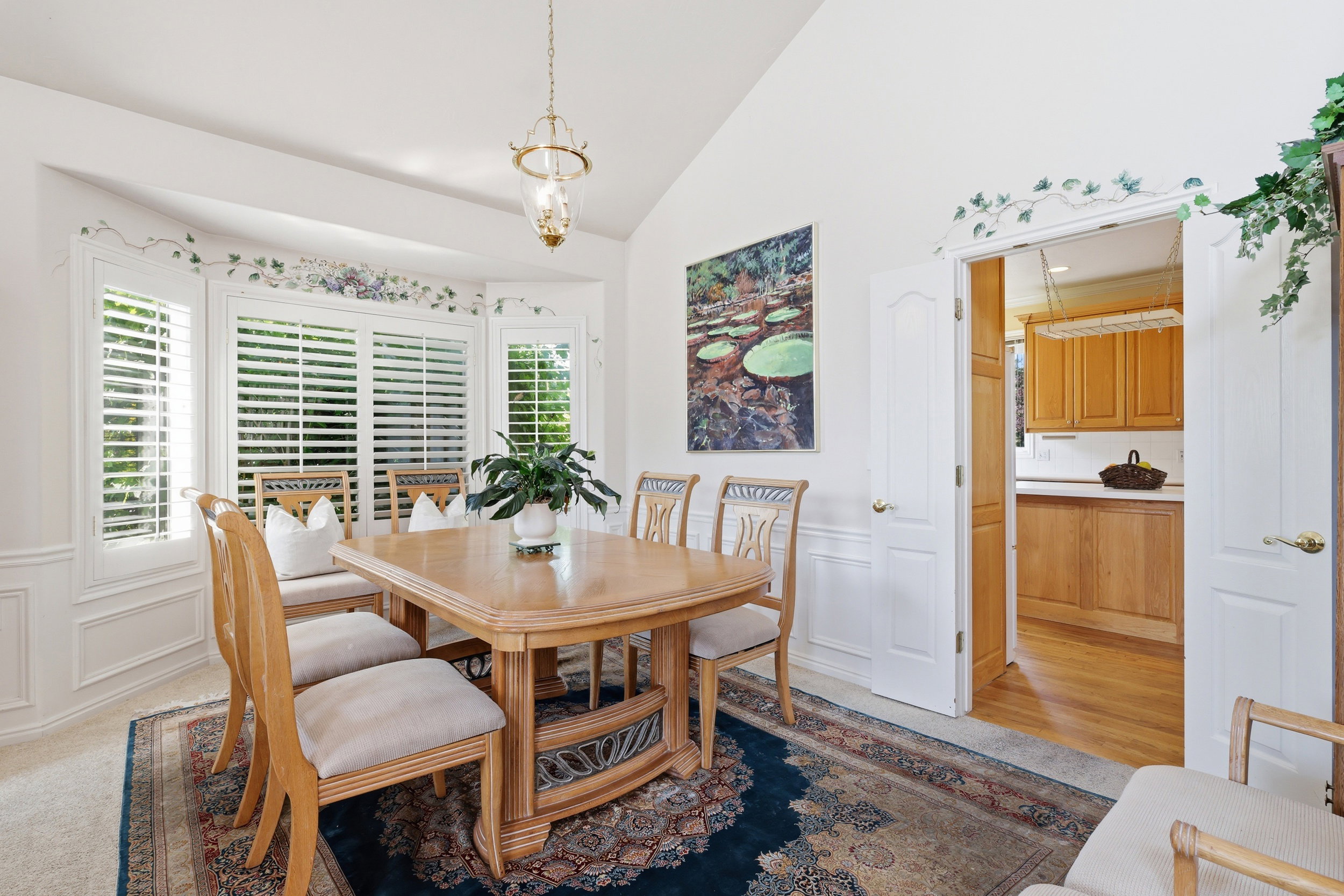 Formal dining space featuring a bay window with plantation shutters, wainscoting, and a vaulted ceiling