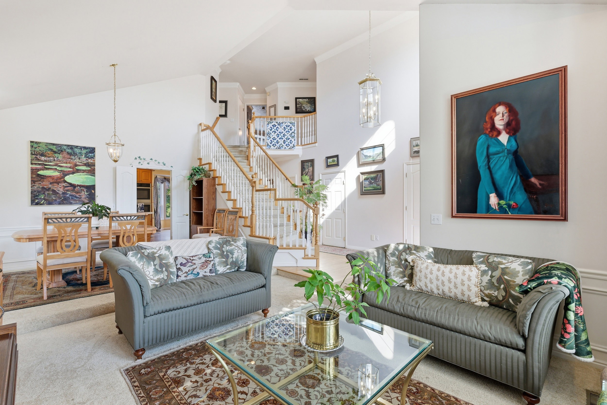 Two-story foyer featuring a grand staircase with white balusters and wood handrails, vaulted ceilings, and a formal dining area with chandelier lighting