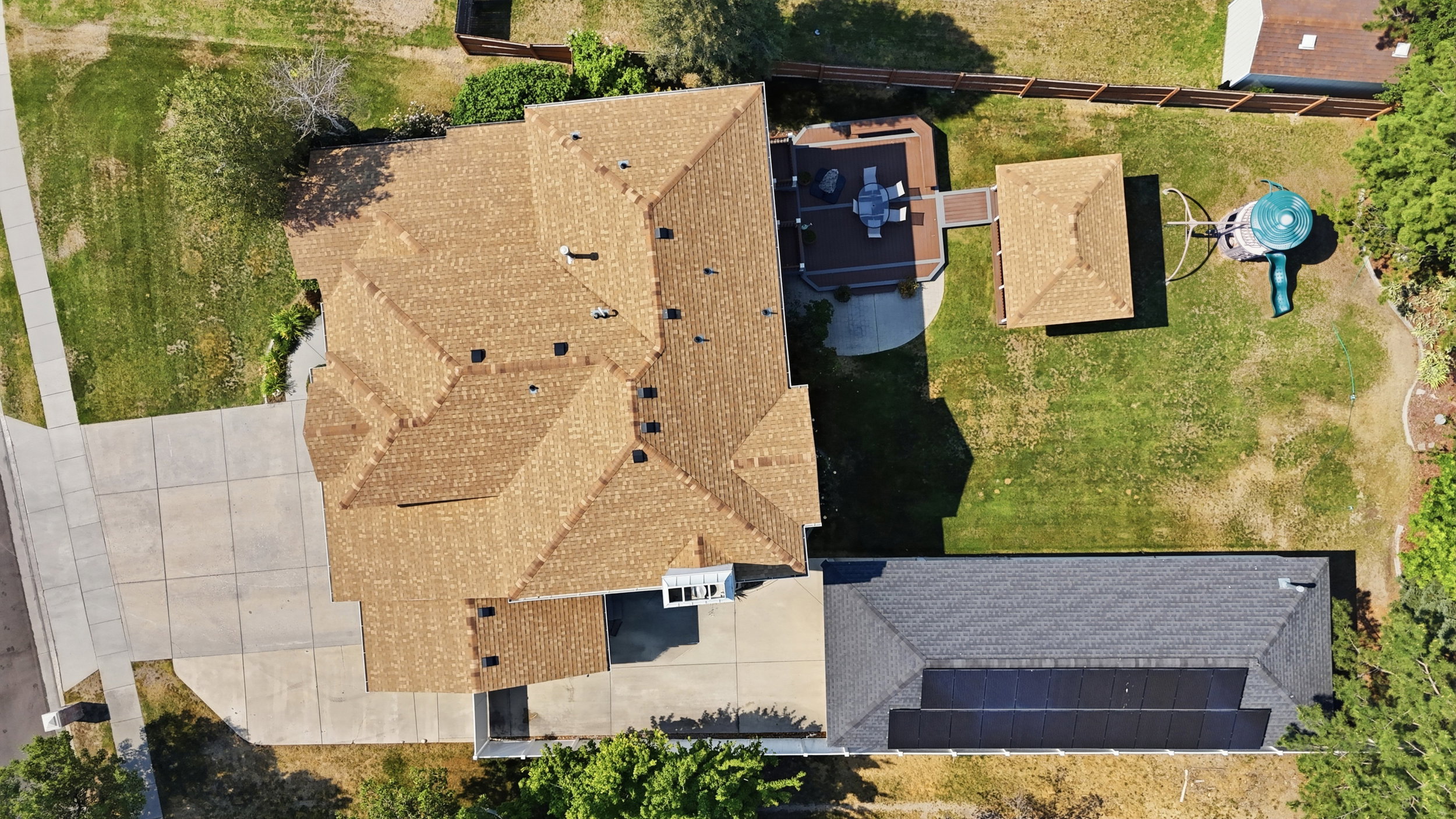 Expansive property featuring a multi-gabled shingle roof, a generously sized concrete driveway, a rear deck with pergola, a separate garage structure, and solar panel installation