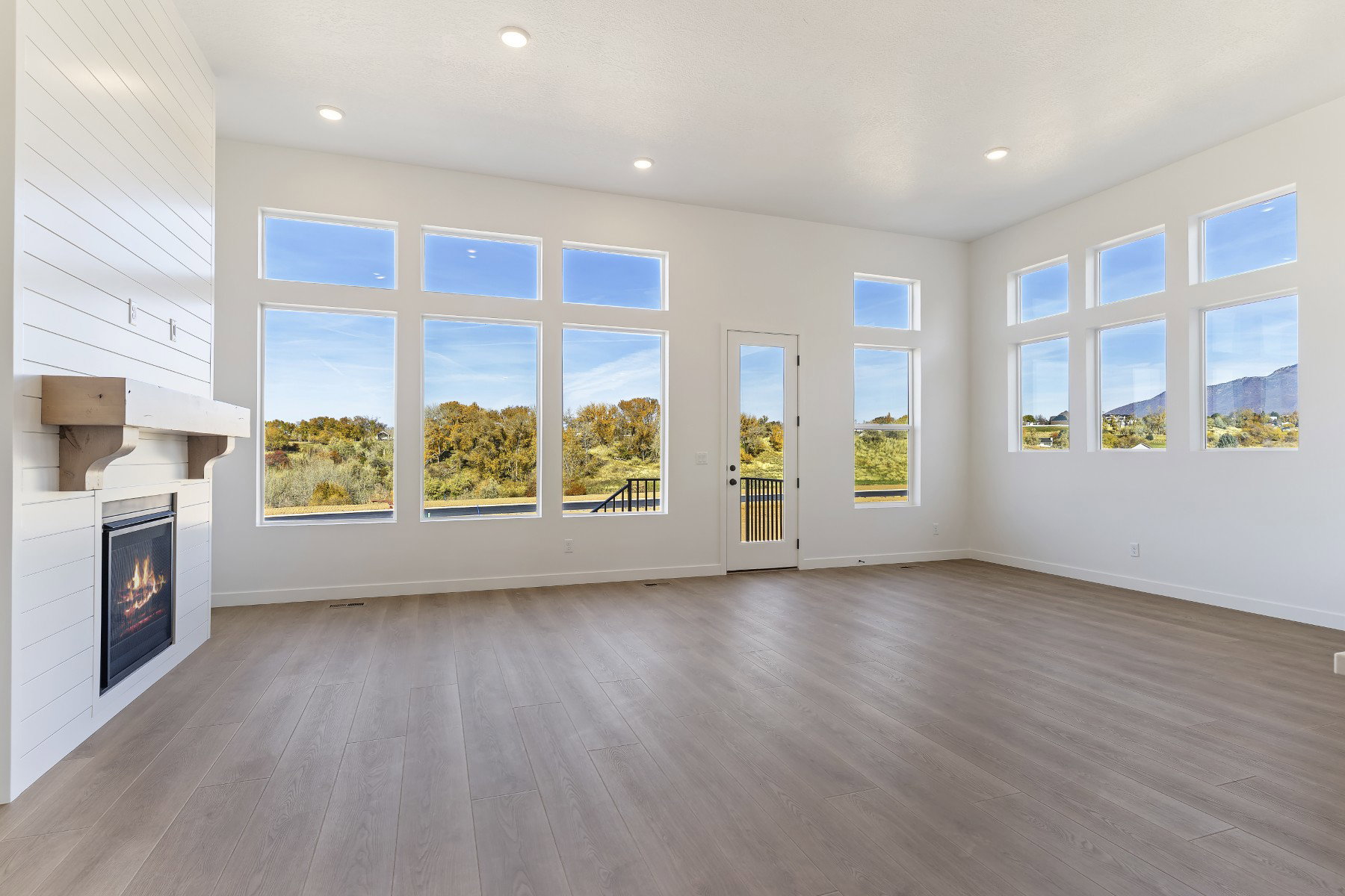 Spacious living area featuring extensive window panels, wood-finish flooring, a contemporary fireplace with a shiplap surround, and a wooden mantel