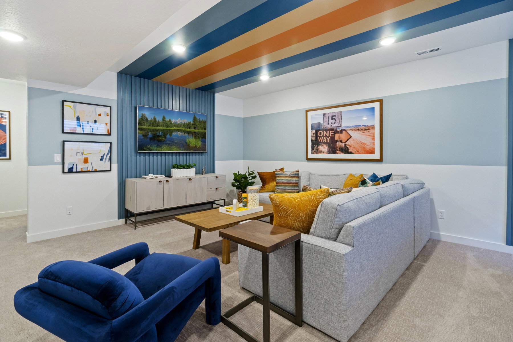 Recessed lighting illuminates a carpeted living space featuring a unique ceiling design with blue and orange stripes