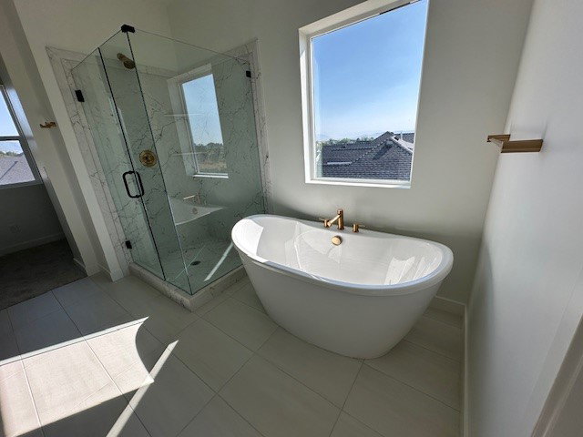 Bathroom featuring a freestanding tub with brass fixtures, a glass-enclosed shower with marble-look tile, and a built-in shower bench