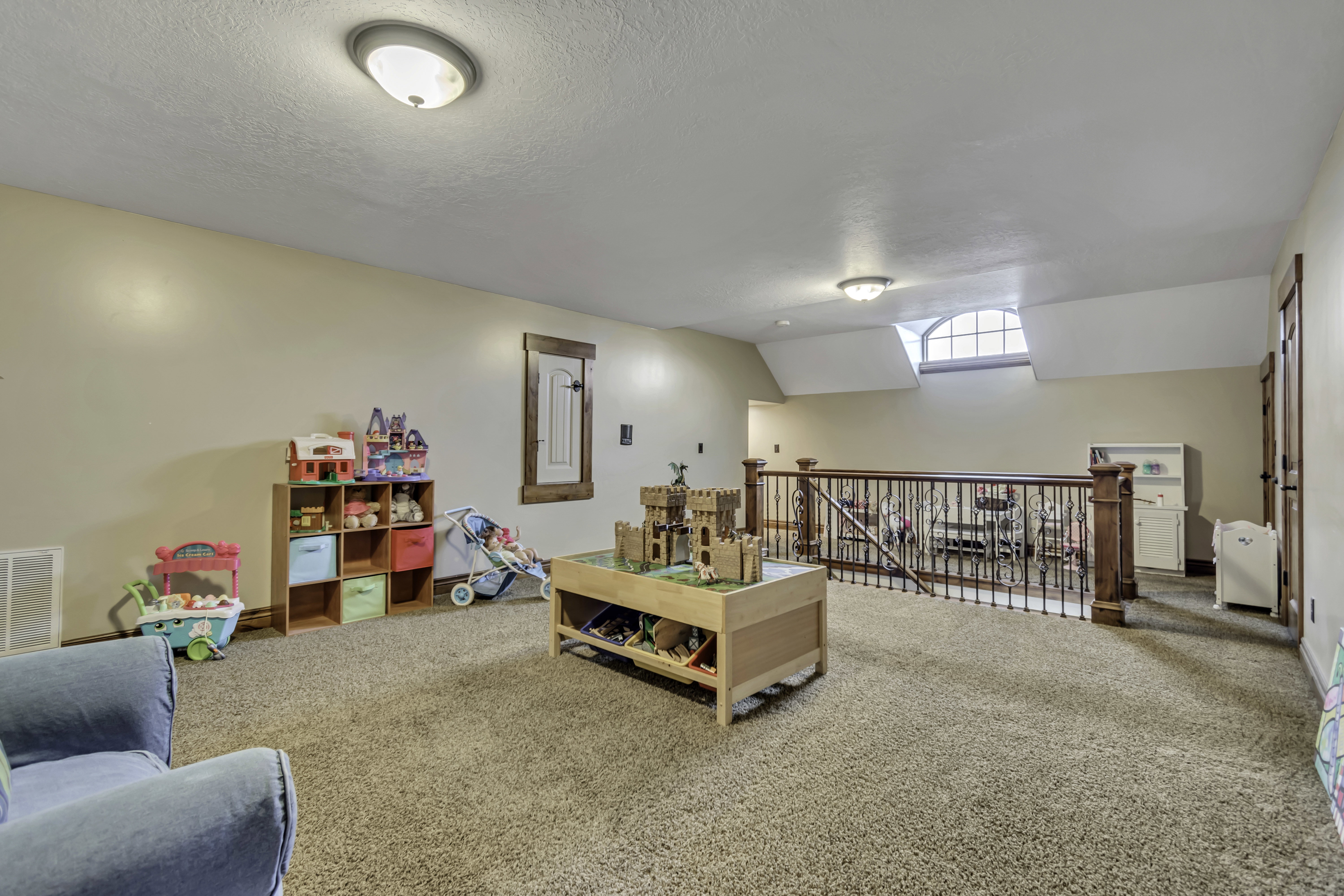 Carpeted bonus room featuring a wood railing with metal spindles, an arched dormer window, and two flush mount ceiling lights