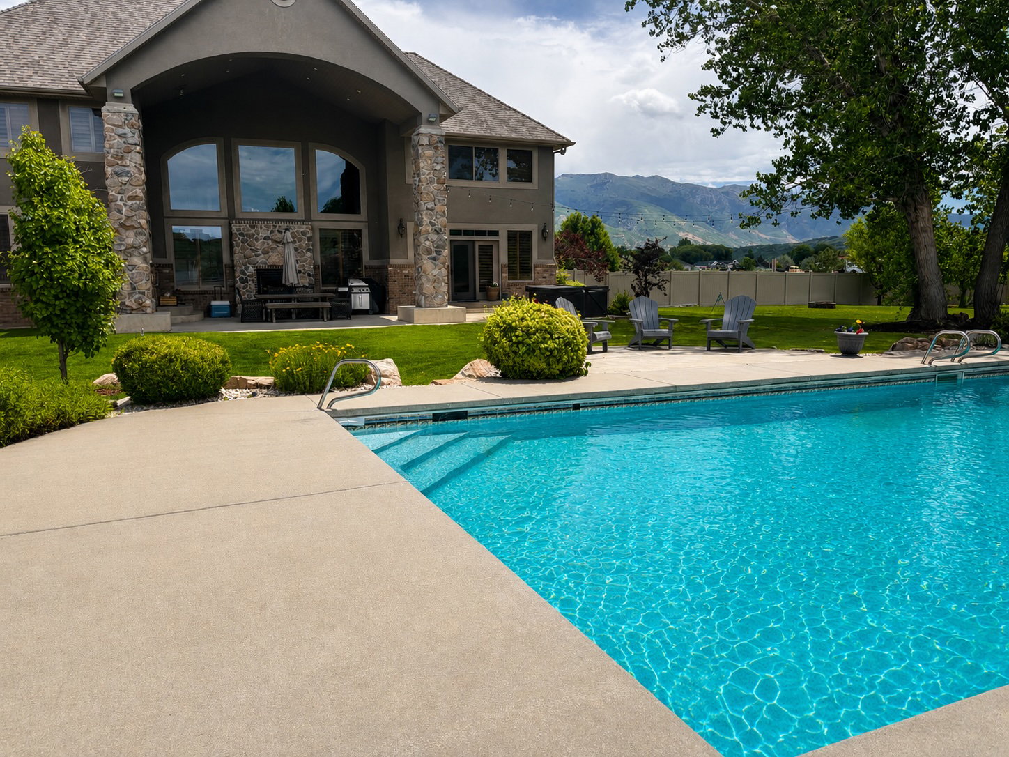 In-ground swimming pool with concrete decking, surrounded by a manicured lawn and mature trees