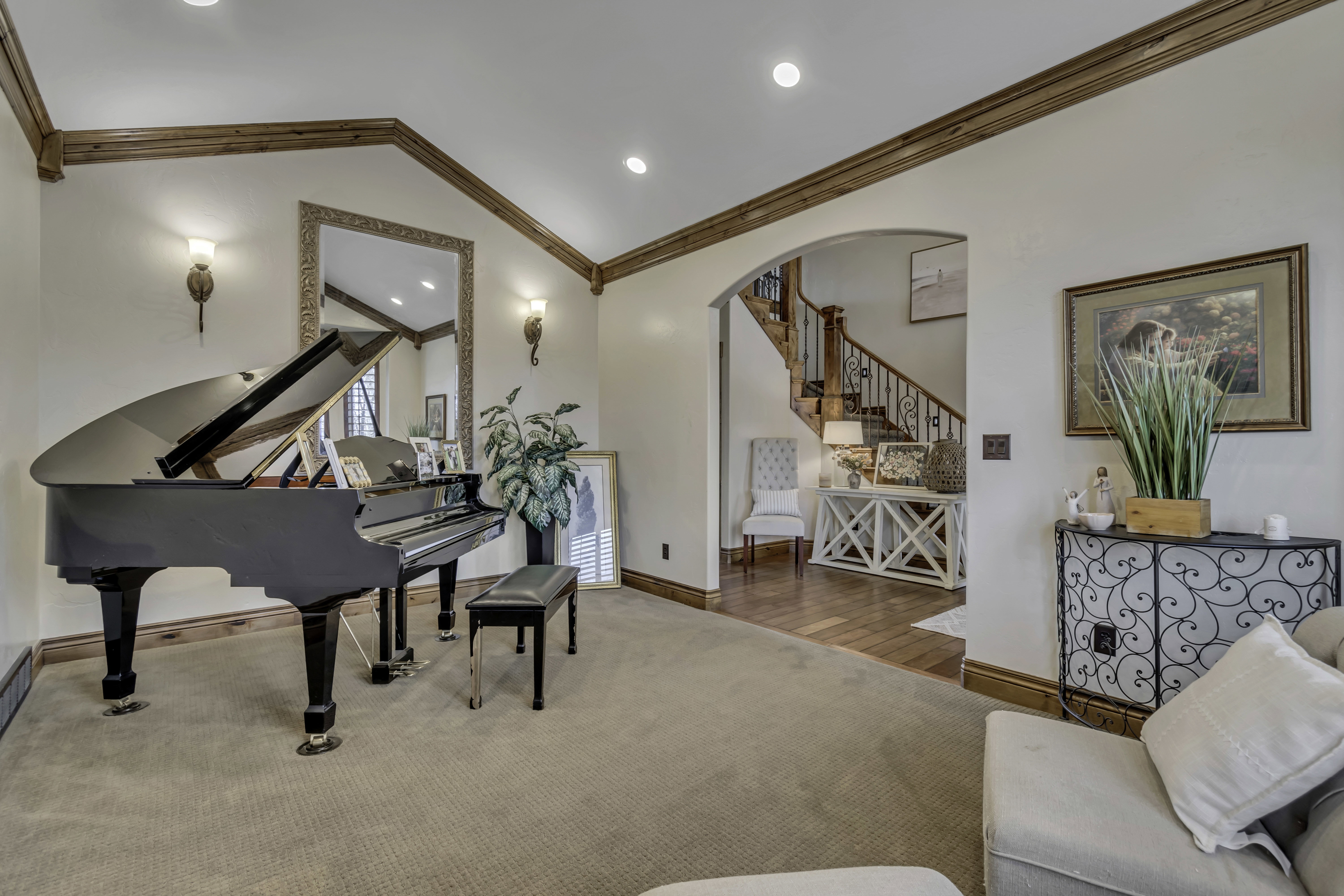 Formal living space with neutral carpeting, crown molding, wall sconces, recessed lighting, and a broad arched entryway to the foyer