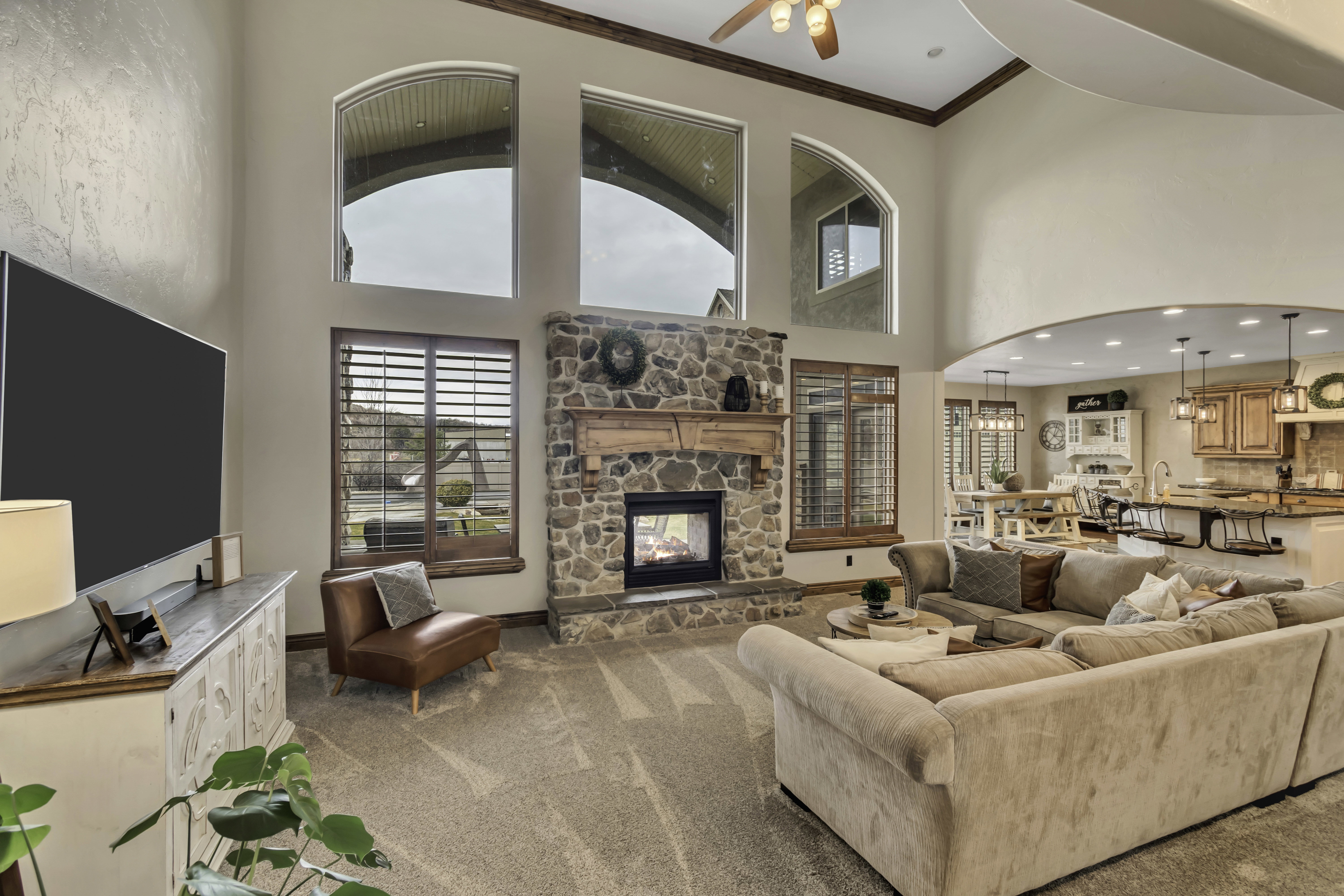 Two-story living area featuring a stone fireplace with a wood mantel, vaulted ceilings with wood beams, and a ceiling fan