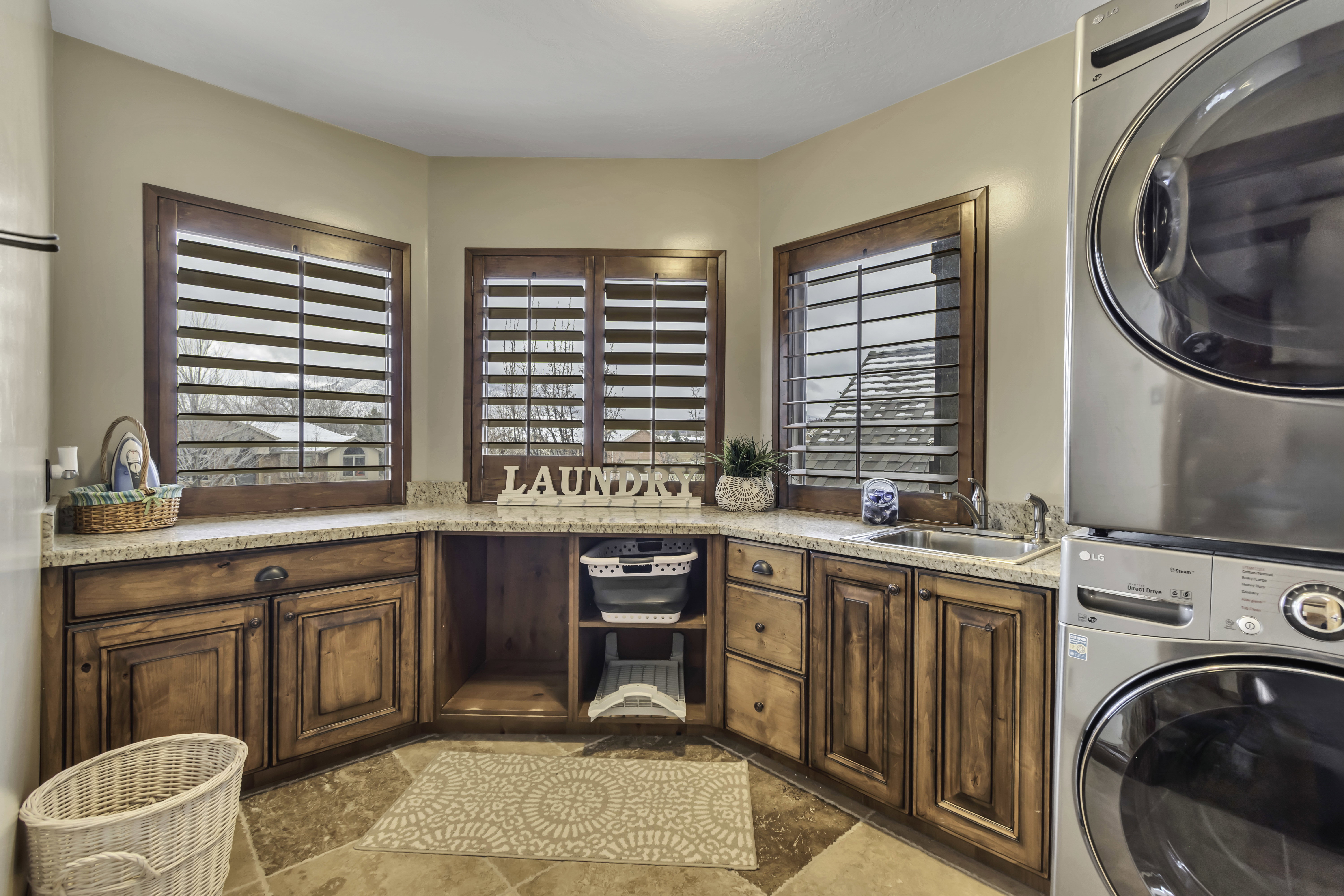 Dedicated laundry area featuring granite countertops, custom wood cabinetry, tiled flooring, and a stainless steel utility sink