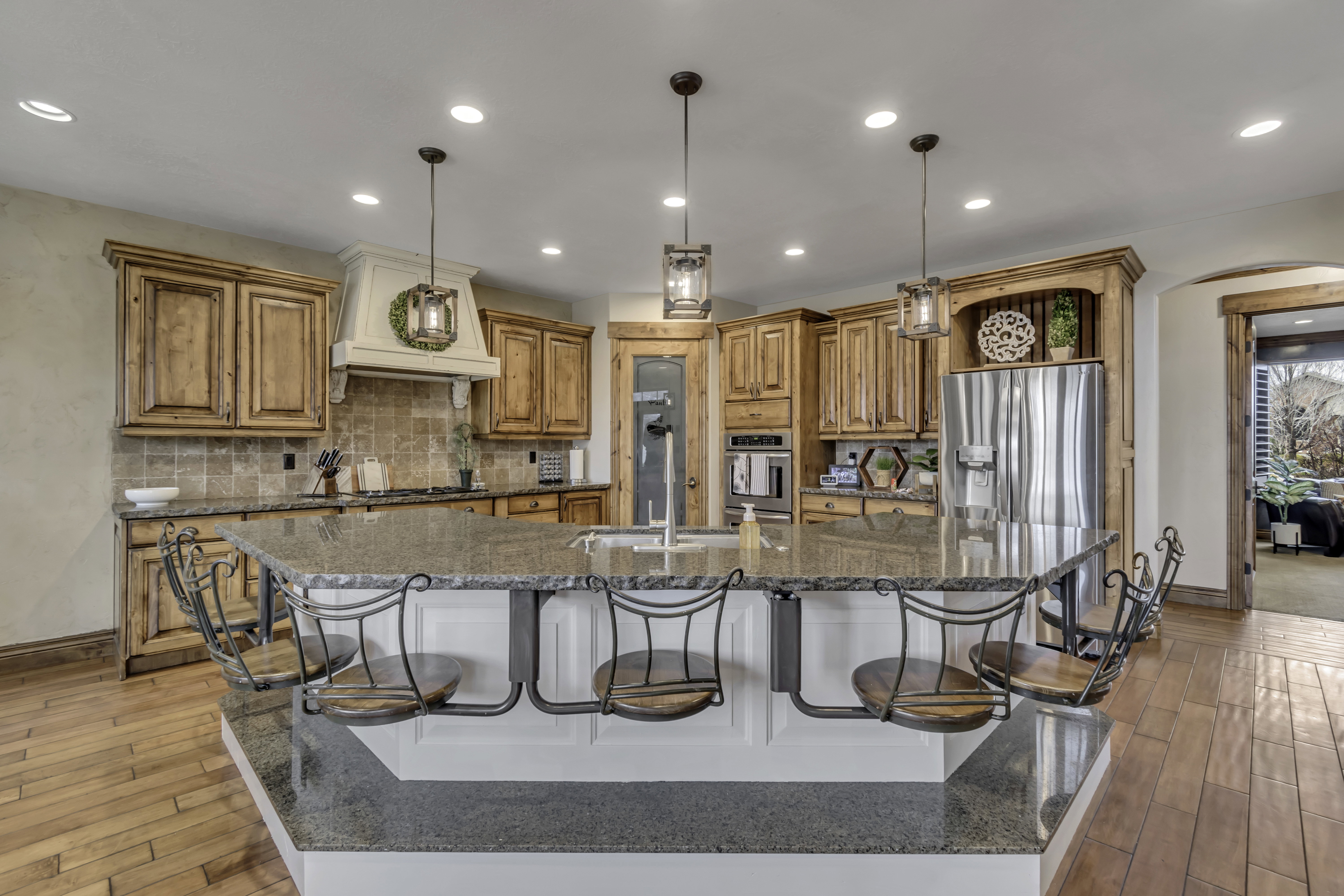 Spacious kitchen featuring a large multi-level island with seating, natural wood cabinetry, stainless steel appliances, a tiled backsplash, and recessed lighting