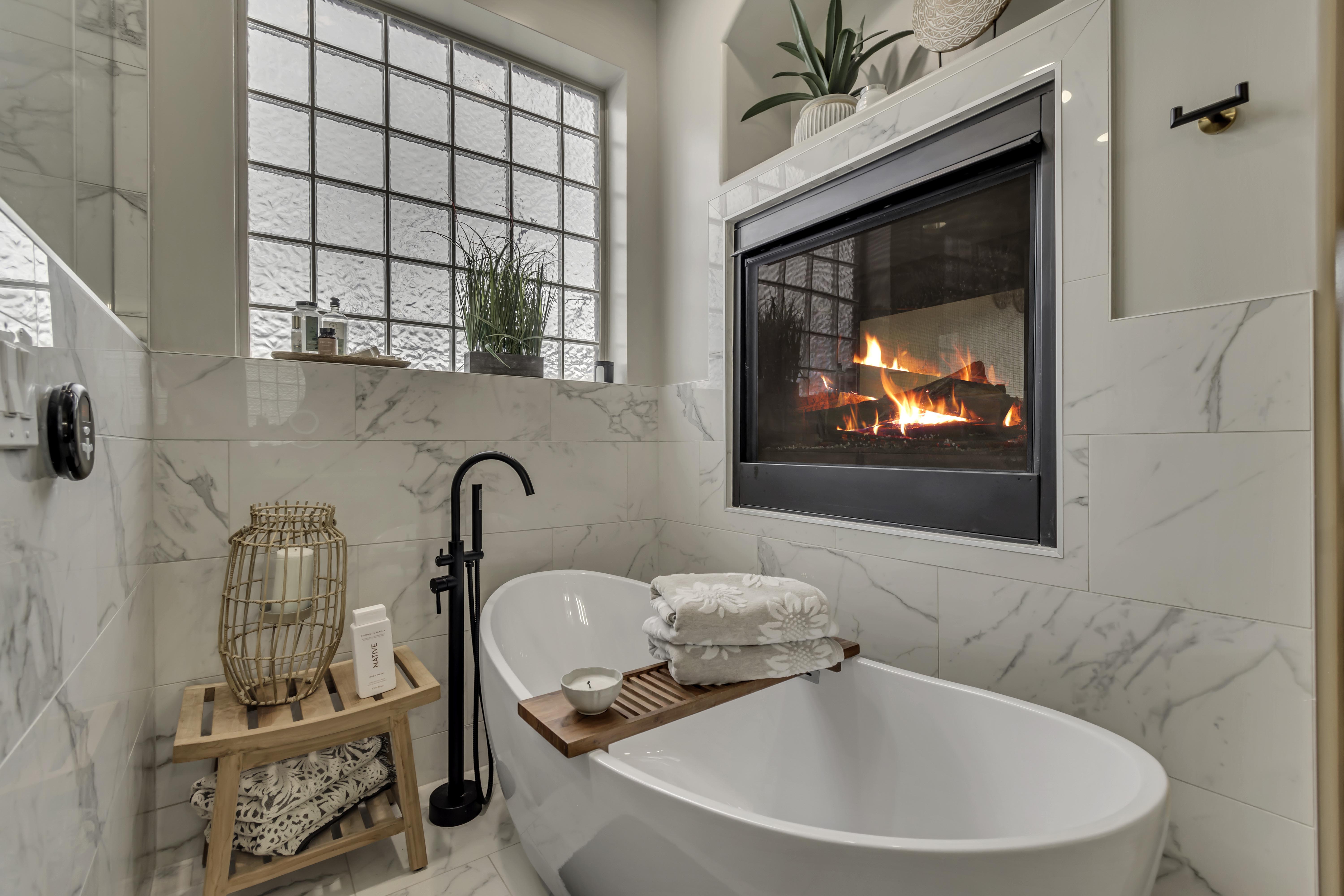Freestanding soaking tub with a floor-mounted matte black faucet, surrounded by large format marble-look wall tiling